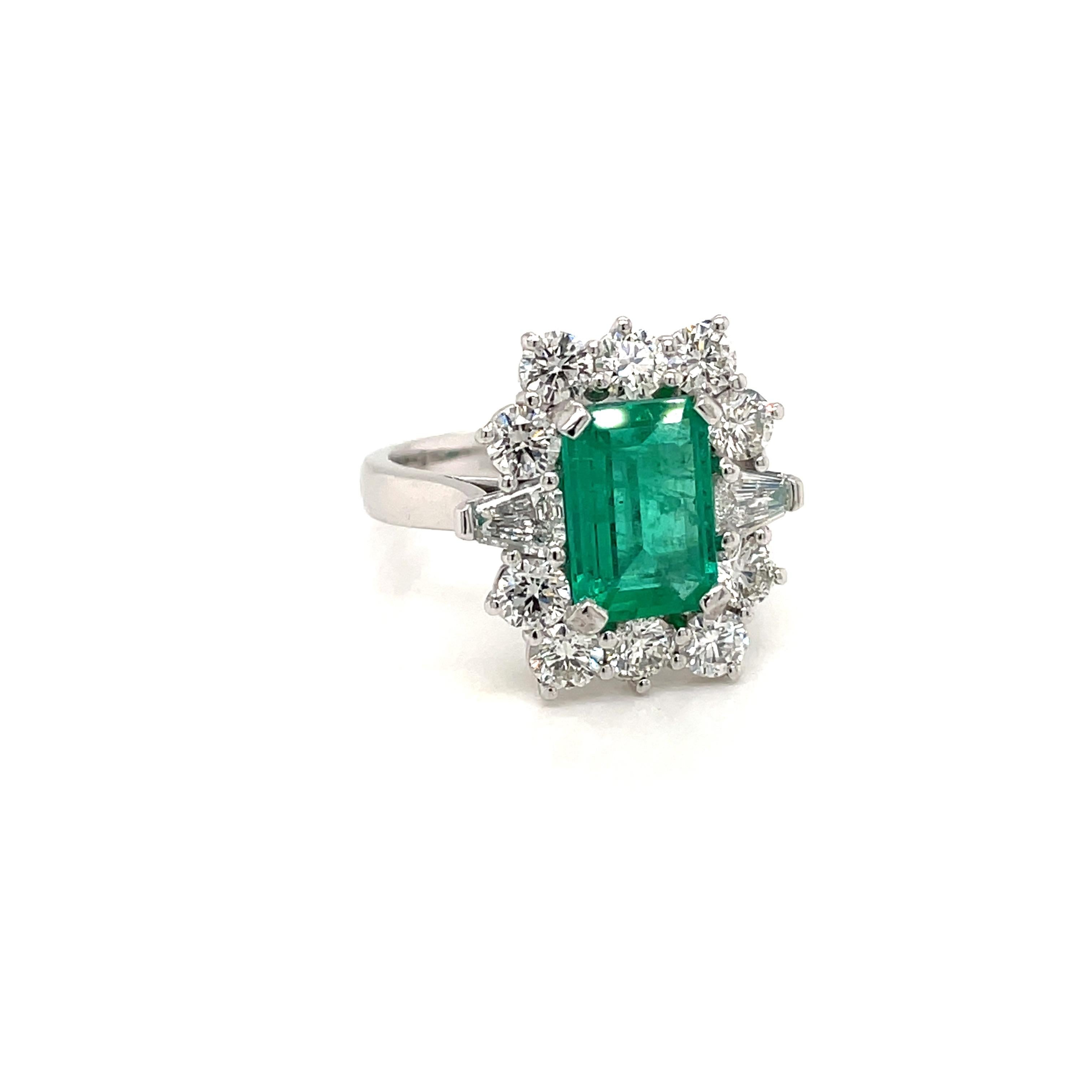 A beautiful and impressive Platinum Gold engagement ring showcasing a natural Vivid Colombian Emerald 2.50 carats of great quality, surrounded by  10 Sparkling Round brilliant cut diamonds and two trapezoid cut on the sides, total weight 2.70