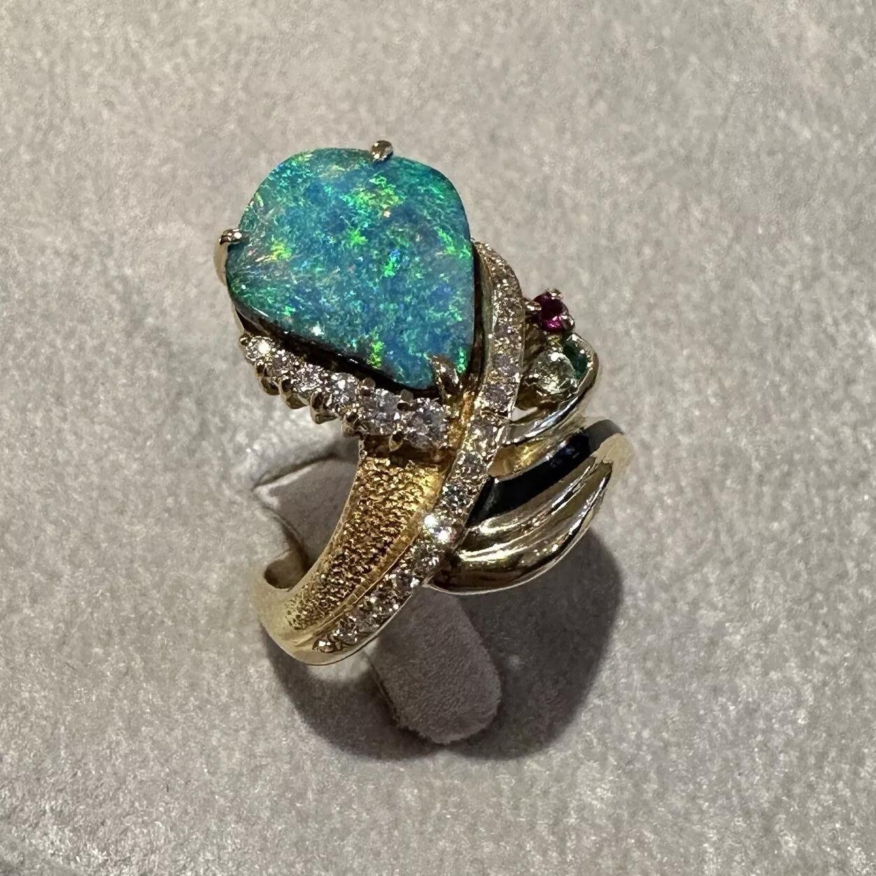 Estate Boulder Opal Ring with Diamonds in 18k Yellow Gold 

Boulder Opal Ring features one Pear shaped Boulder Opal with color play of Blue, Green, and flashes of Orange accented with Round Brilliant Diamonds and three color gemstones, all set in a