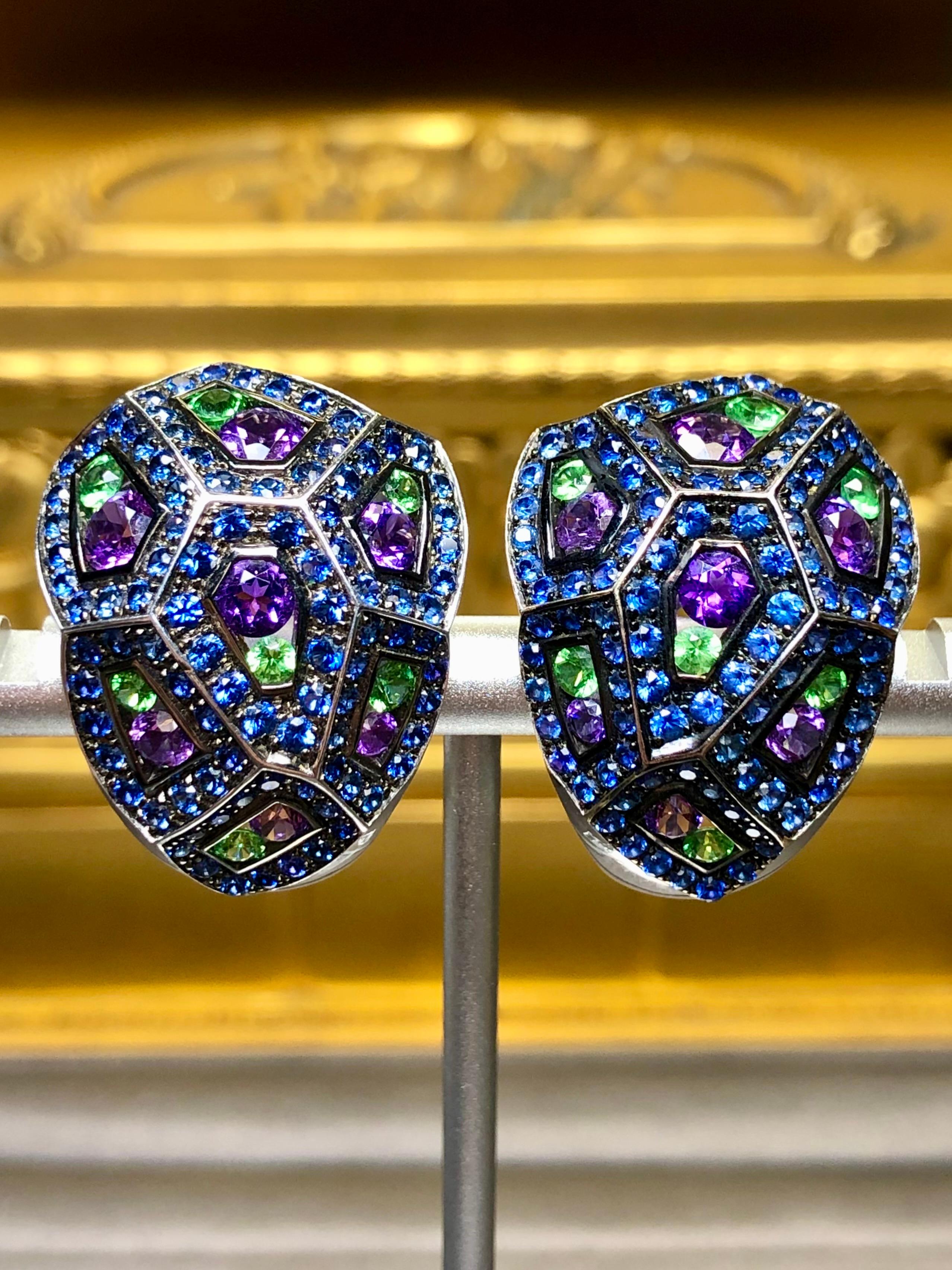 An absolutely gorgeous pair of geometric design huggie earrings by Carl Bucherer done in 18K white gold. They have been set with approximately 9.60cttw in sapphires, 1.80cttw in tsavorites and 2.80cttw in amethyst. Truly an eye catching and bold