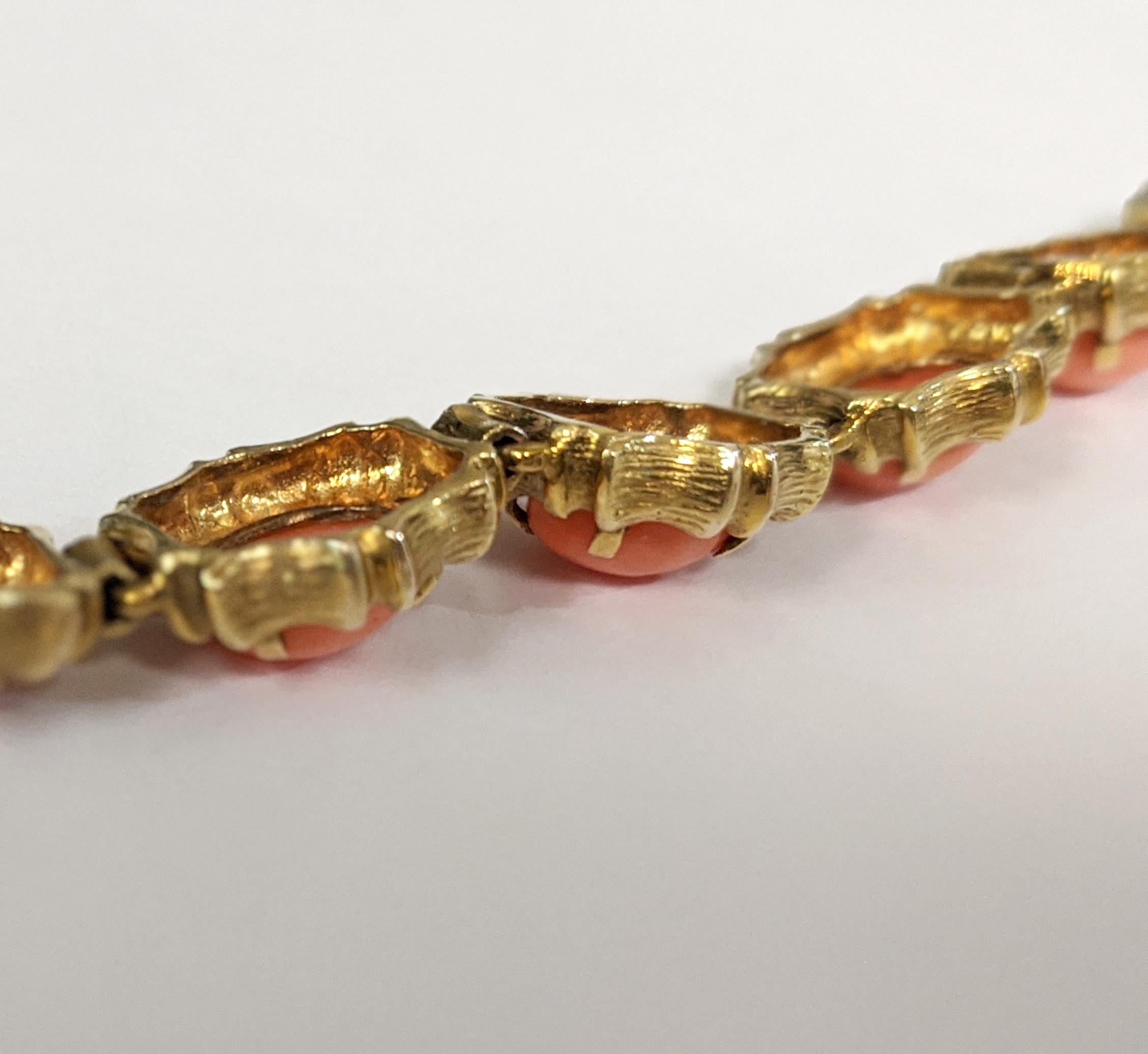 Salmon-colored corals glow in this 14 K yellow gold bracelet. The stone settings are finely detailed with a wood-carved texture. 

The bracelet contains ten oval cabochon corals. Approximately 7.5 inches in length, with an easy-close box clasp and
