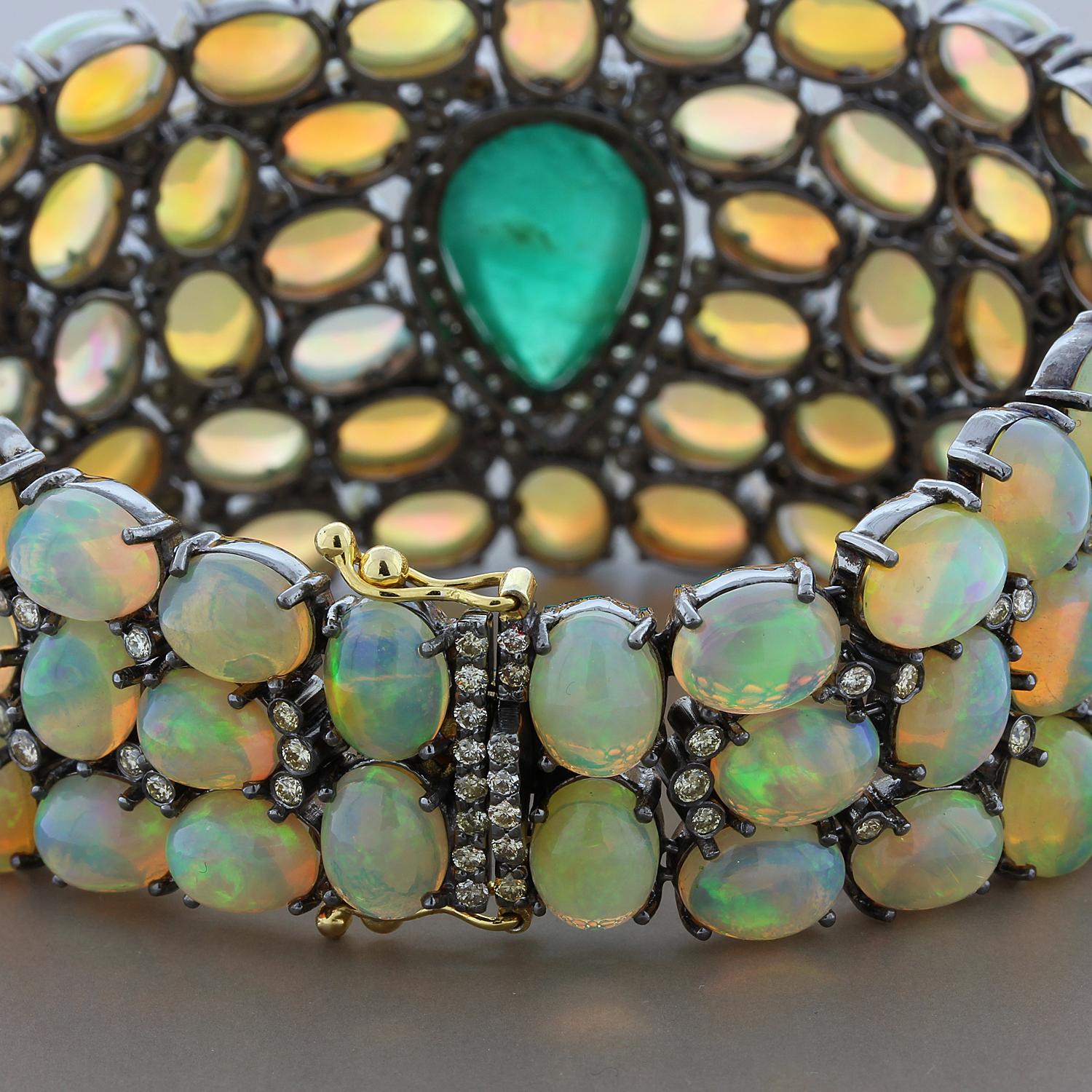 A bold 6 carat pear cut cabochon emerald takes center stage of this exceptional bracelet. The deep green emerald is surrounded by 100 carats of vibrant opals with beautiful play of color. The emerald is haloed by 2.19 carats of diamonds with bezel