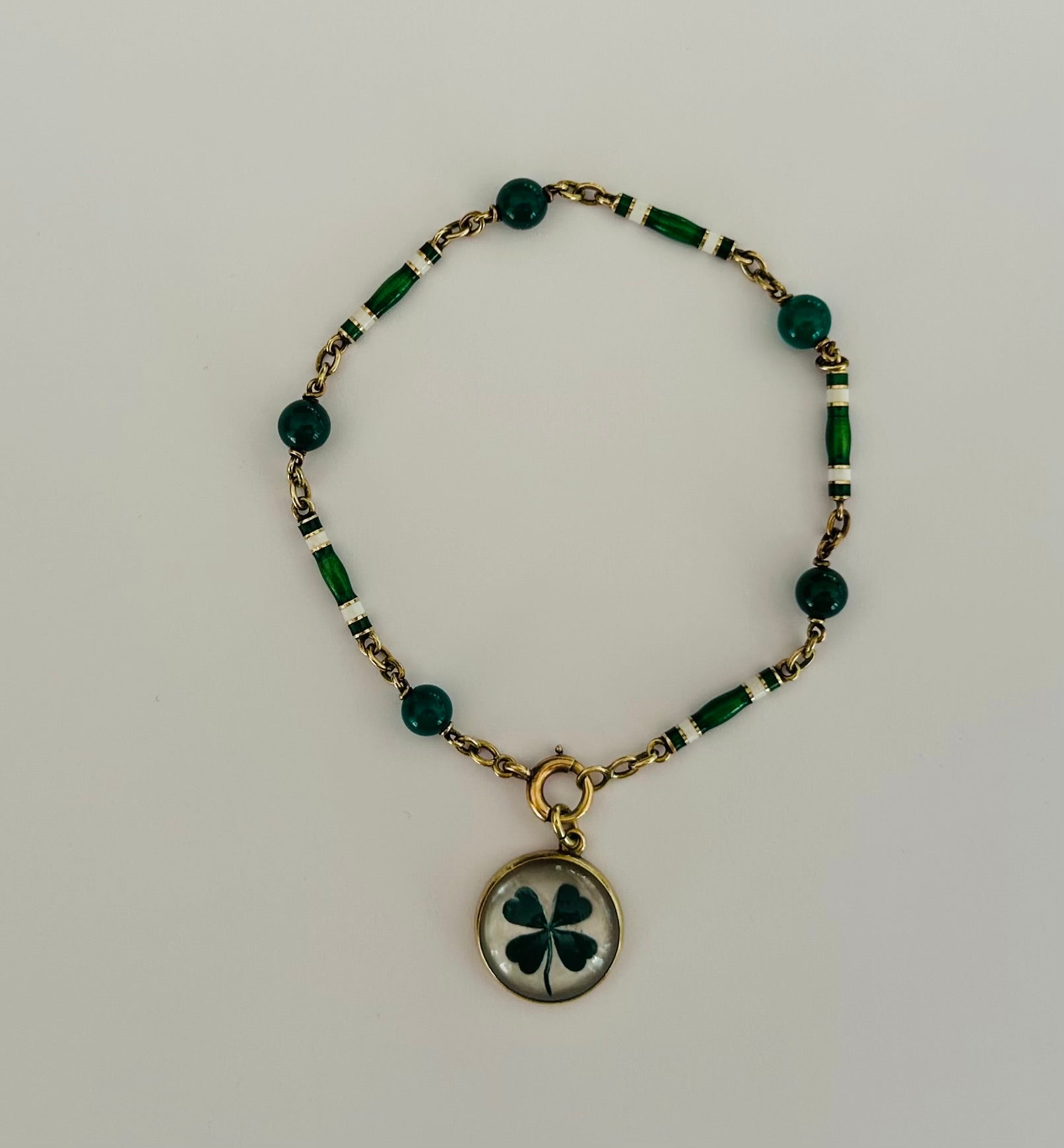 Crafted in the 1970s, this Estate Irish charm bracelet features green and white enamel links interspersed with green chrysoprase beads measuring approximately 5.3mm each that can be worn with or without a detachable four-leaf clover charm. Set in