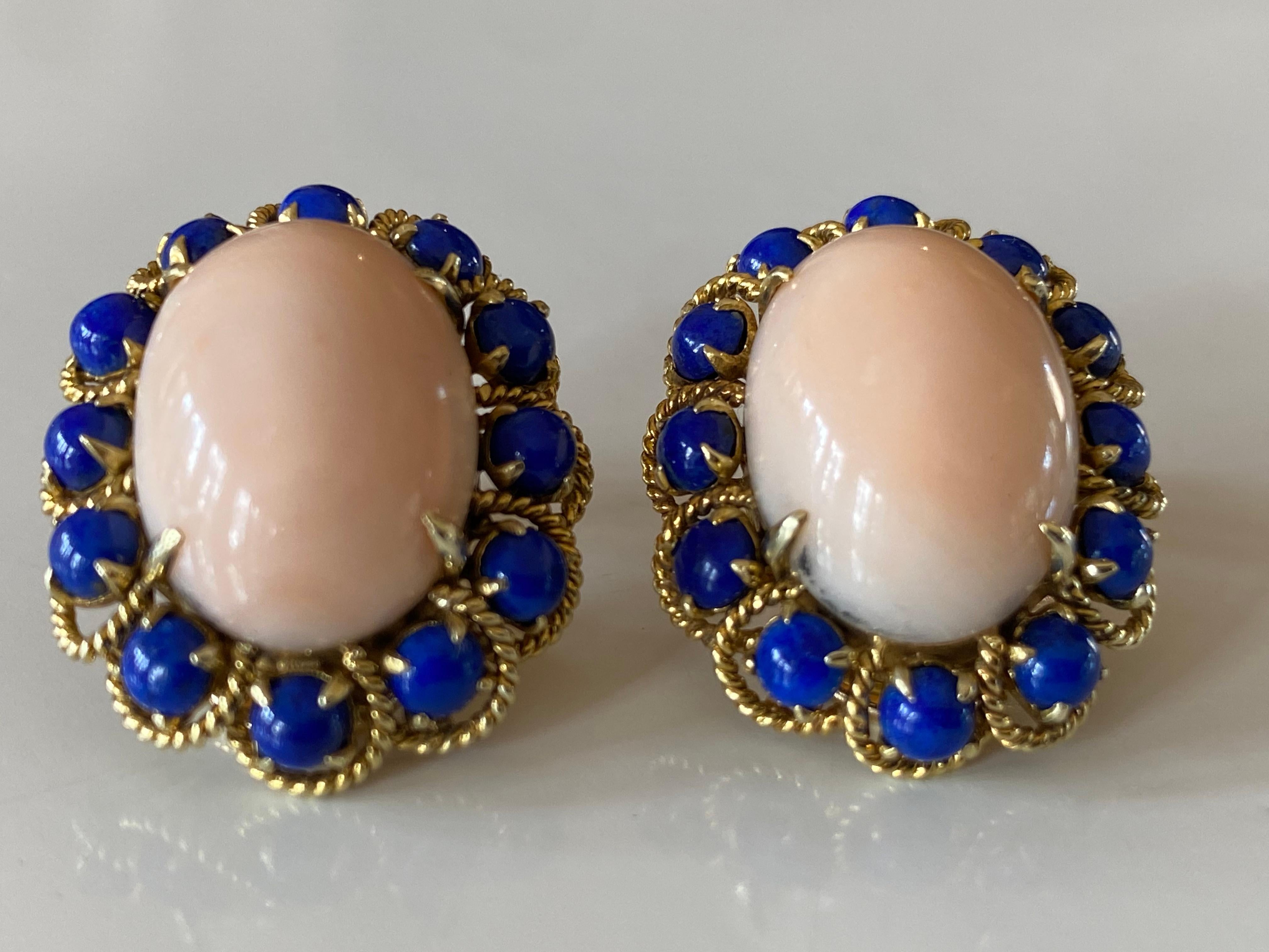 Crafted in the 1950s in 14kt yellow gold, these stunning clip on earrings each feature a natural angel skin coral oval-shaped cabochon measuring approximately 12 x 18mm encircled by twelve natural round lapus lazuli stones and secured with omega