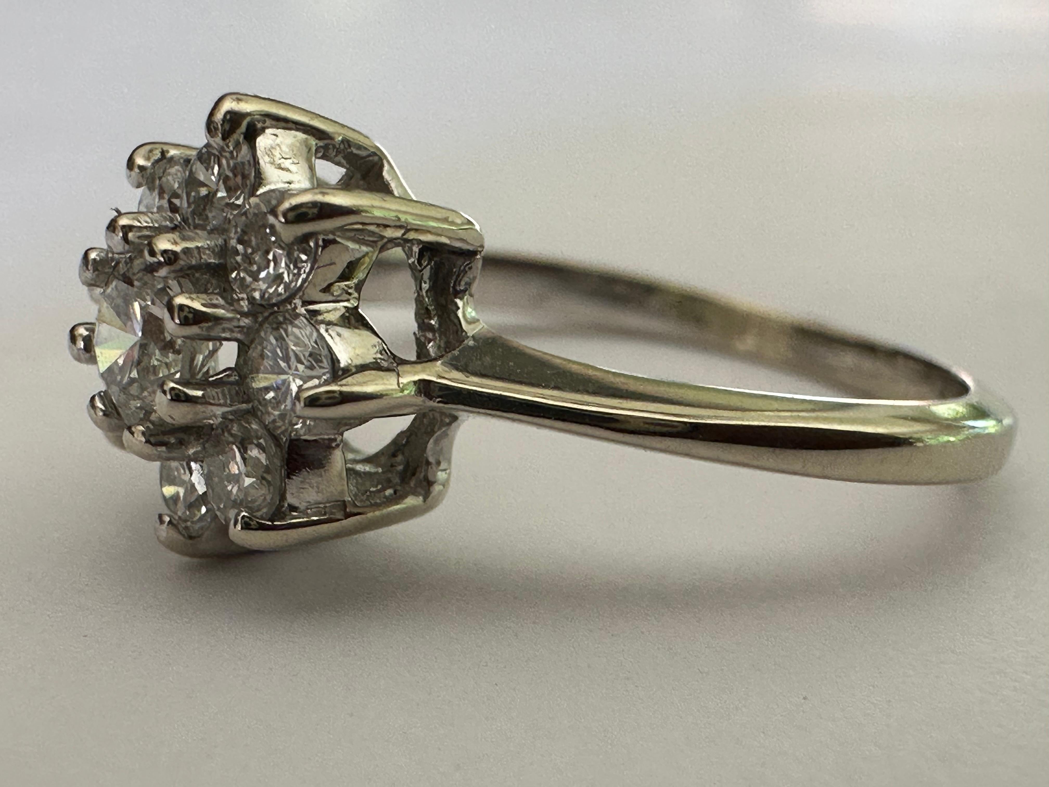 This stunning ring forms an elegant eight-petal flower bejeweled with round brilliant cut diamonds and centered with a round brilliant-cut diamond measuring approximately 0.20 carat, F color VS clarity. Set in 14K white gold. 

