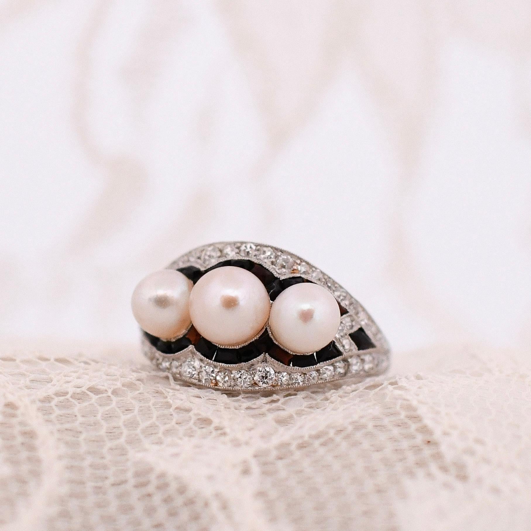 Step into the glamour of the Art Deco period with this exquisite platinum band ring. Adorned with three lustrous pearls that exude timeless elegance, the ring is accentuated by a dazzling diamond and onyx arrangement, creating a captivating contrast