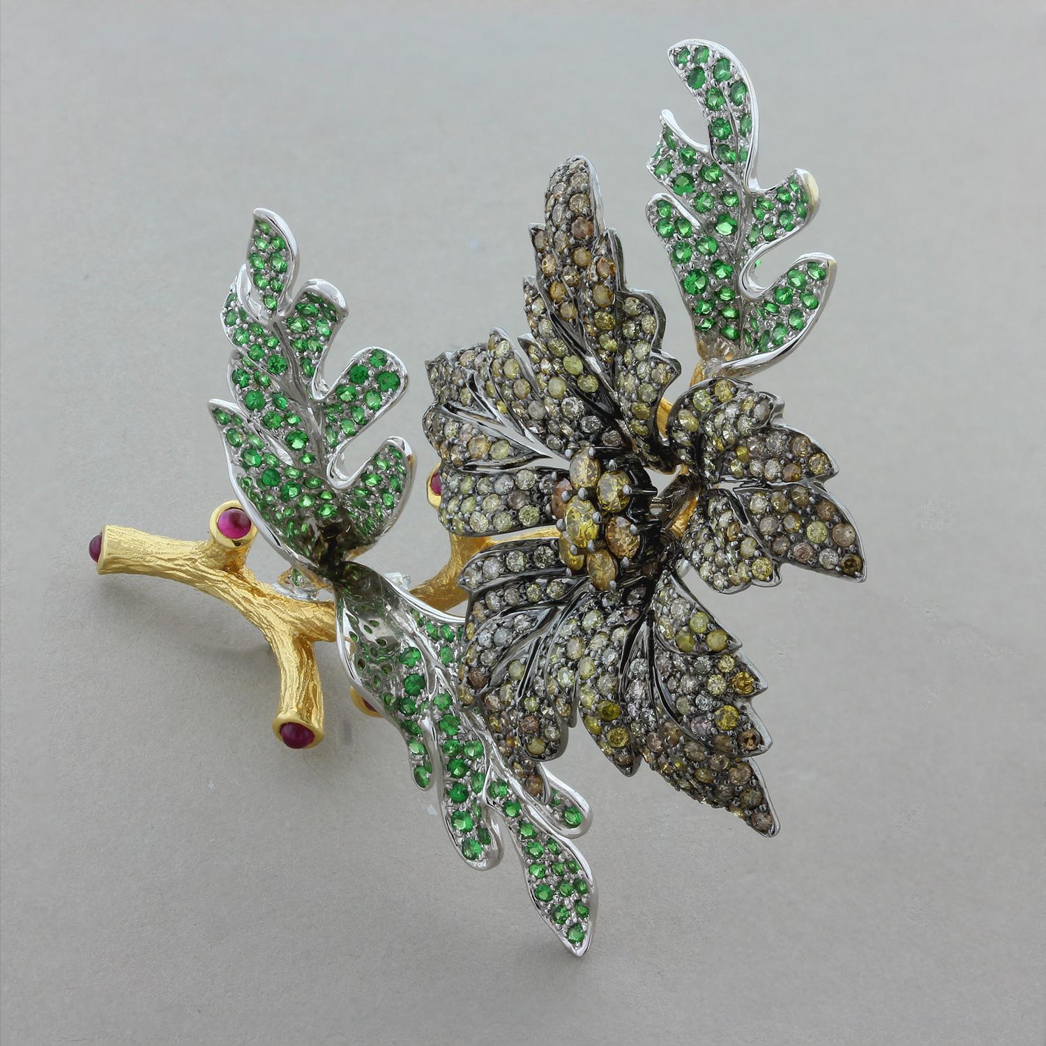 This gorgeously proud flower brooch features approximately 9 carats of fancy colored diamonds for the five petals and bright green tsavorite for the three leaves and red cabochon rubies at the end of each of the five stems. This characterful