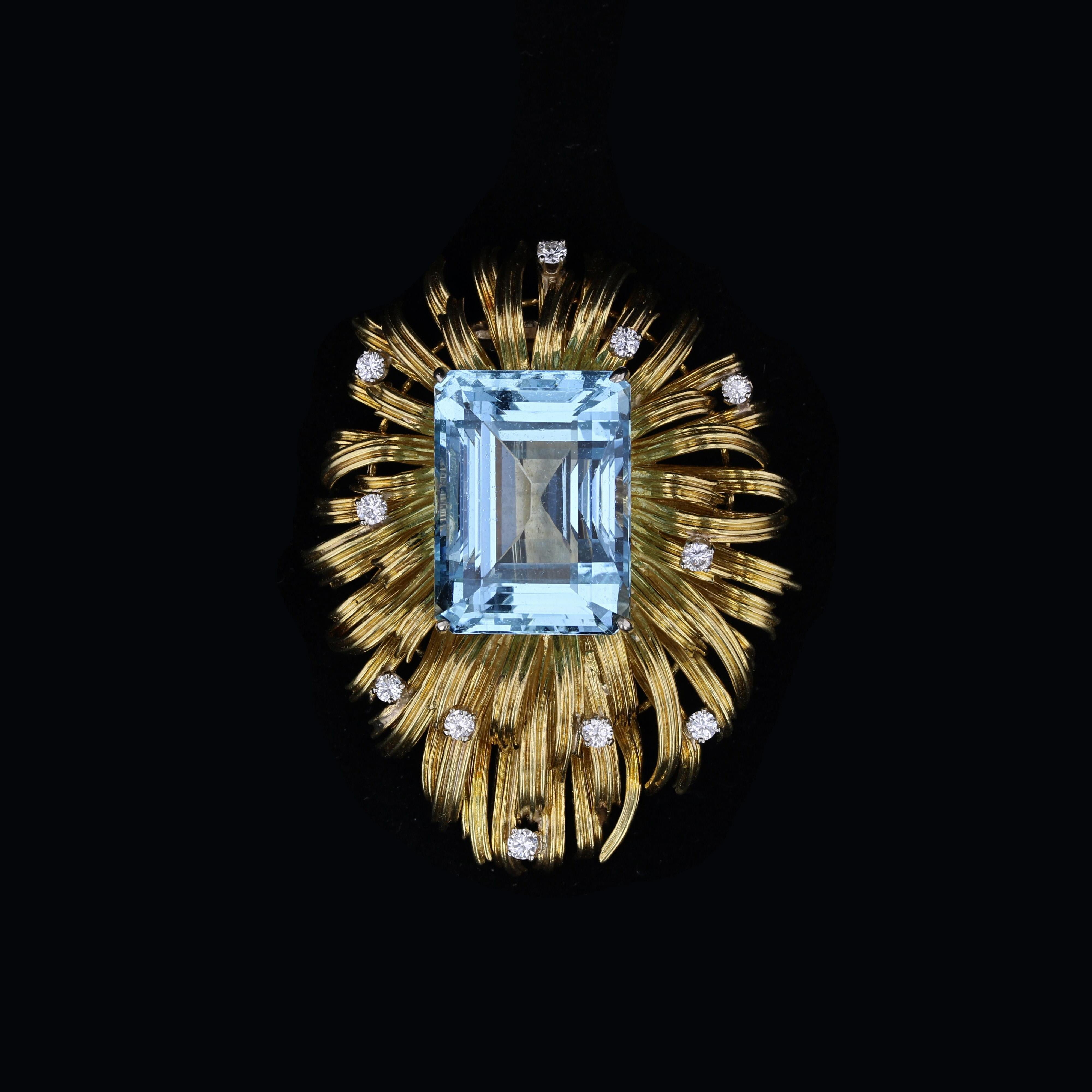 This vibrant 18K yellow gold brooch is centered with an emerald-cut aquamarine weighing in at 10.00 carats. The brooch features a large hidden bail on the reverse side, so the piece can also be worn as a pendant. 

The aquamarine is accented by a