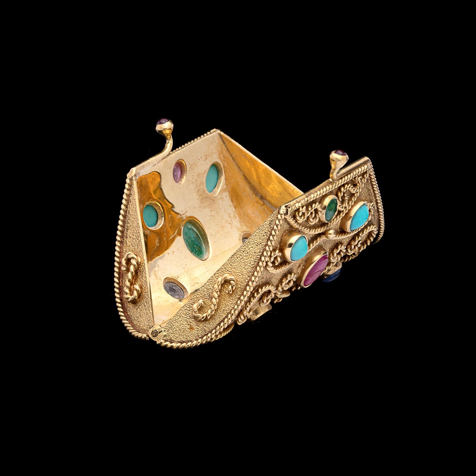 Carry your pills in style! This charming 18k gold clutch purse pill box is designed with elaborate wire work and studded with cabochon and faceted emeralds, rubies, sapphires, and turquoise. Just like a purse, it opens by double tab! It measures