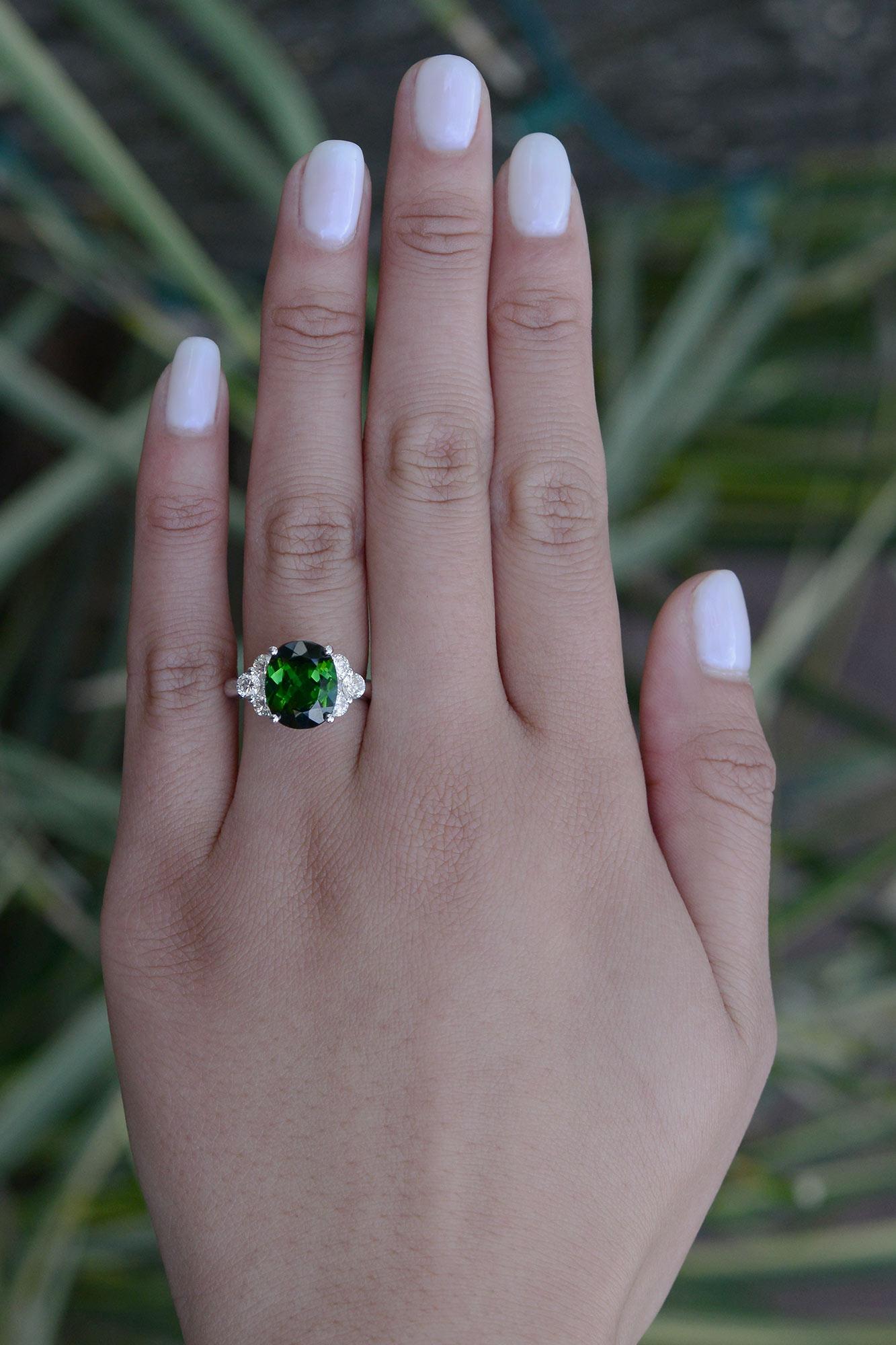 Centered by a rich, deeply saturated forest green tourmaline, this oval gemstone engagement ring is an affordable luxury. The substantial setting is hand crafted of 18kt white gold, holding a glorious gem weighing 4.16 carats, complimented by 1