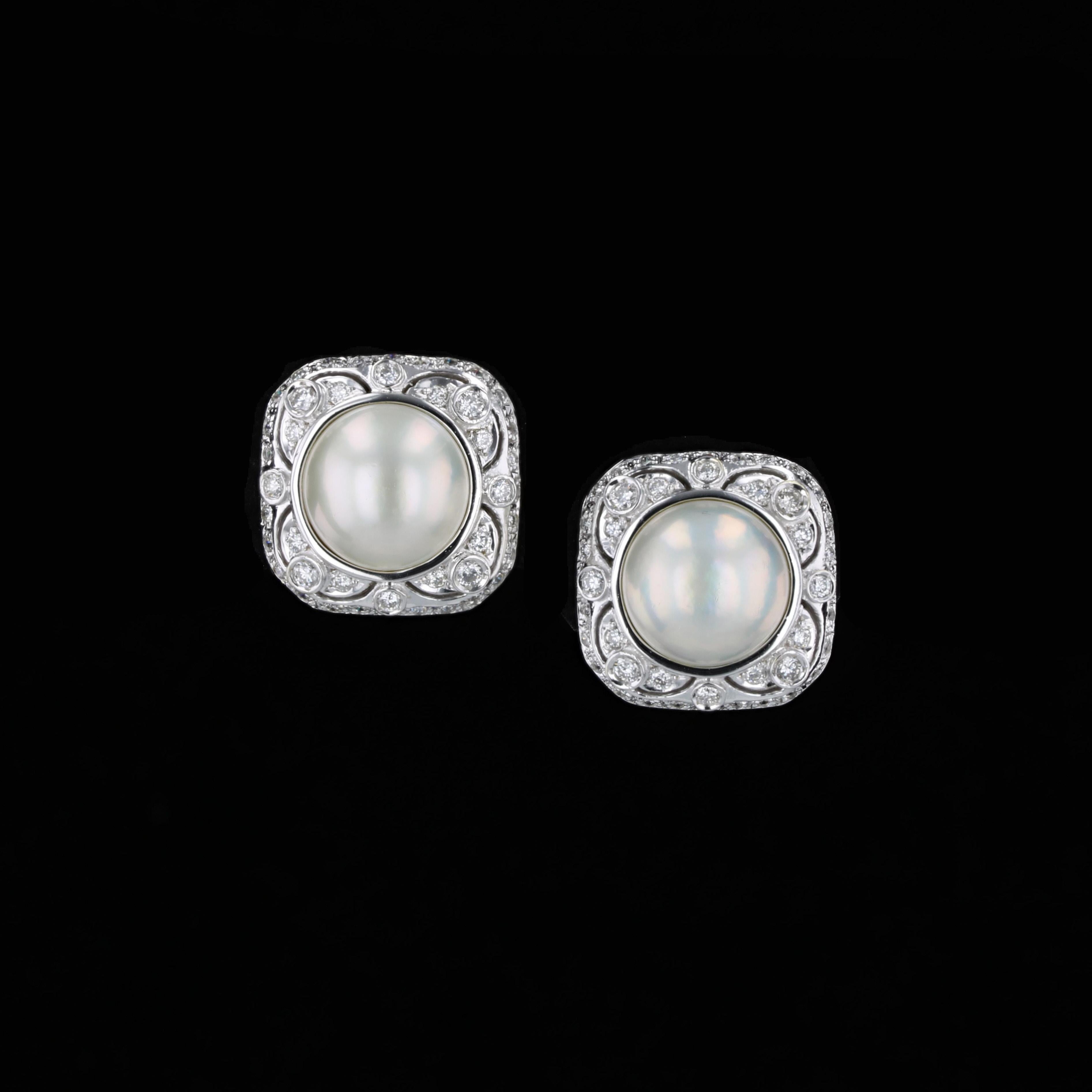 A pair of white mabe pearls measuring 13mm center these estate earrings crafted in 18k white gold. Square button settings glimmer with 80 round brilliant diamonds having average color of H/I and average clarity of SI1. The diamonds have an