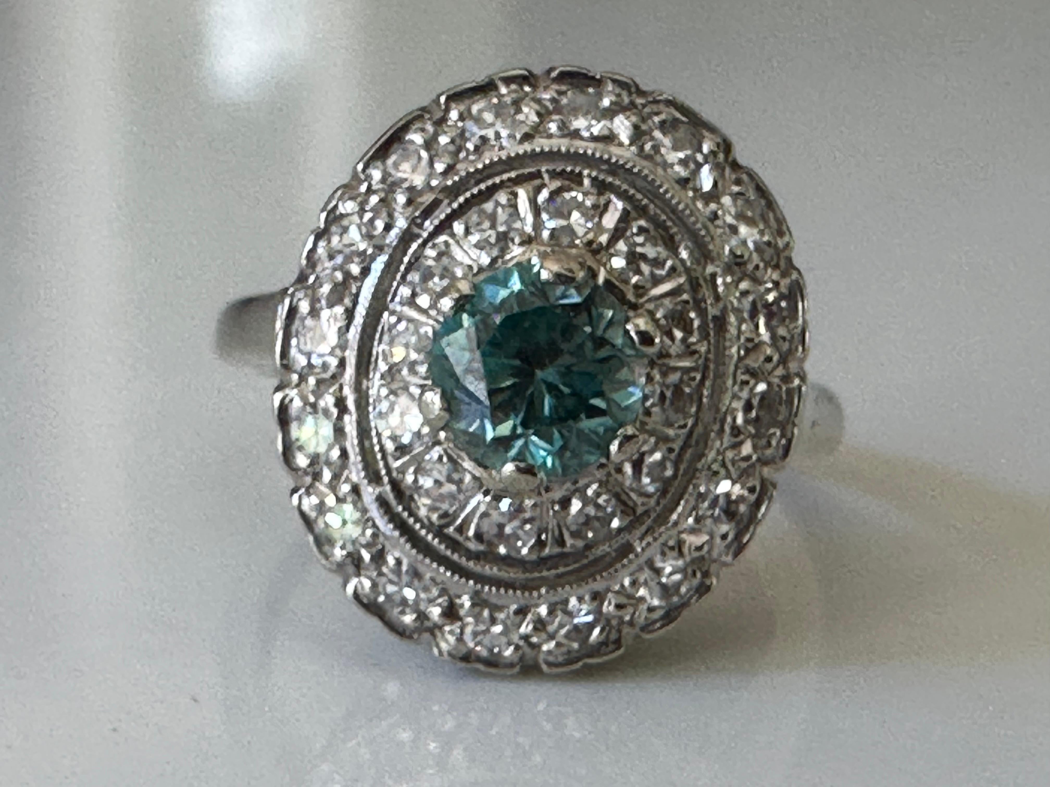 Crafted in the 1950s, this mid-century ring features an electric blue round-cut zircon measuring 5.2x5.1mm. The approximately 1.04-carat stone is encircled by a double halo of twenty-eight  sparkling single cut diamonds measuring approximately 0.80