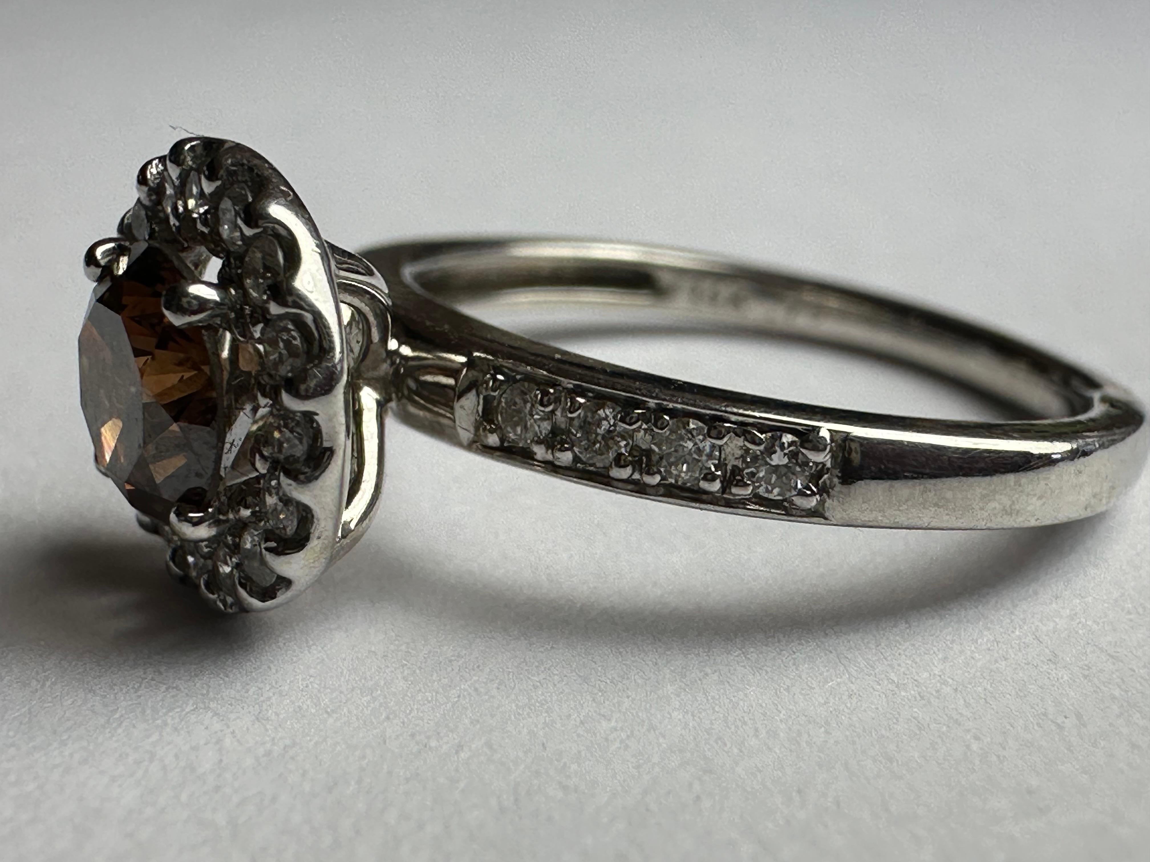 A 0.73-carat round brilliant-cut natural fancy brown or golden-hued diamond, also known as a chocolate diamond, centers this dazzling ring, encircled by a halo of bright white diamonds. Set in 14k white gold. 
