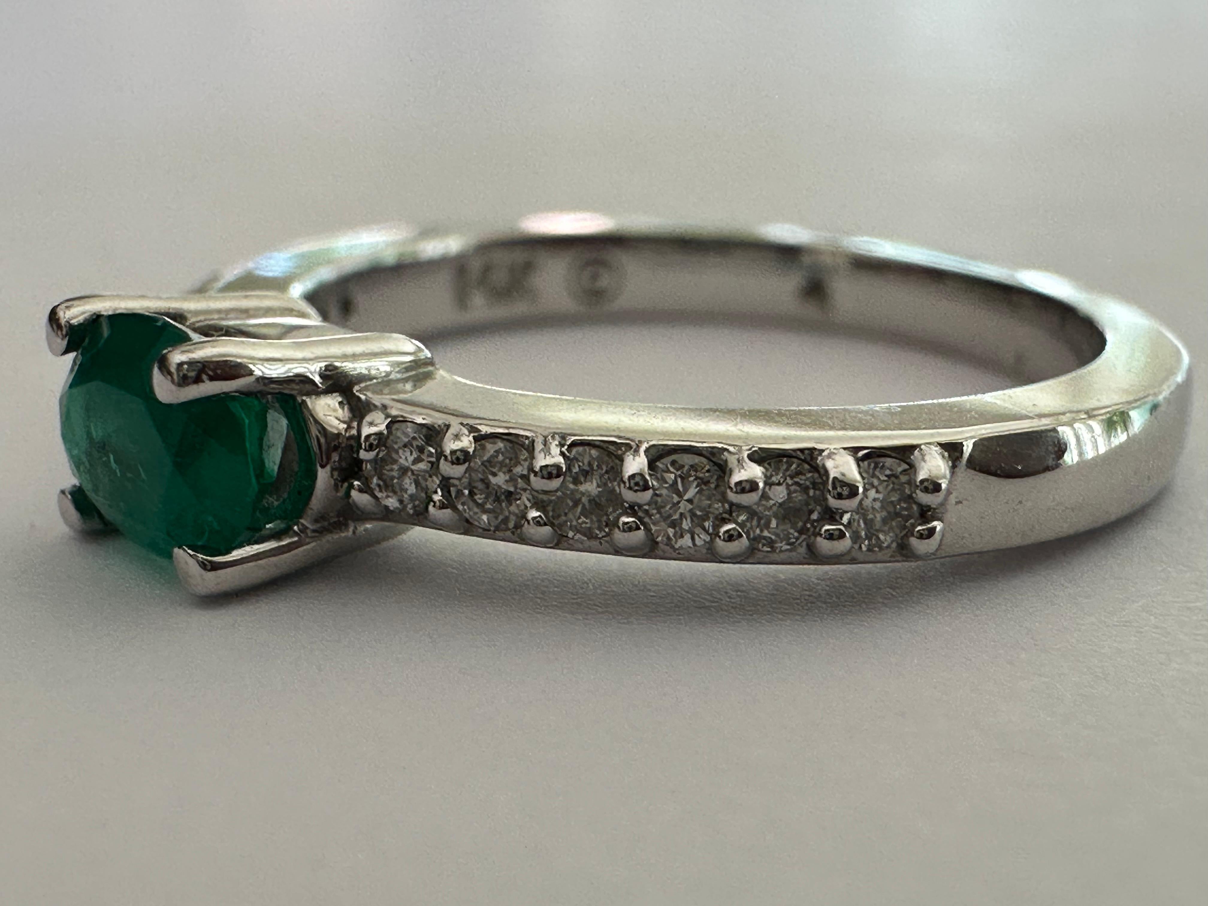 Ein natürlicher ovaler grüner Smaragd von ca. 0,50 Karat steht im Mittelpunkt dieses Ost-West-Estate-Rings, der mit zwölf runden Diamanten, sechs auf jeder Seite, von insgesamt ca. 0,21 Karat akzentuiert ist. Fassung aus 14 Karat Weißgold. 
