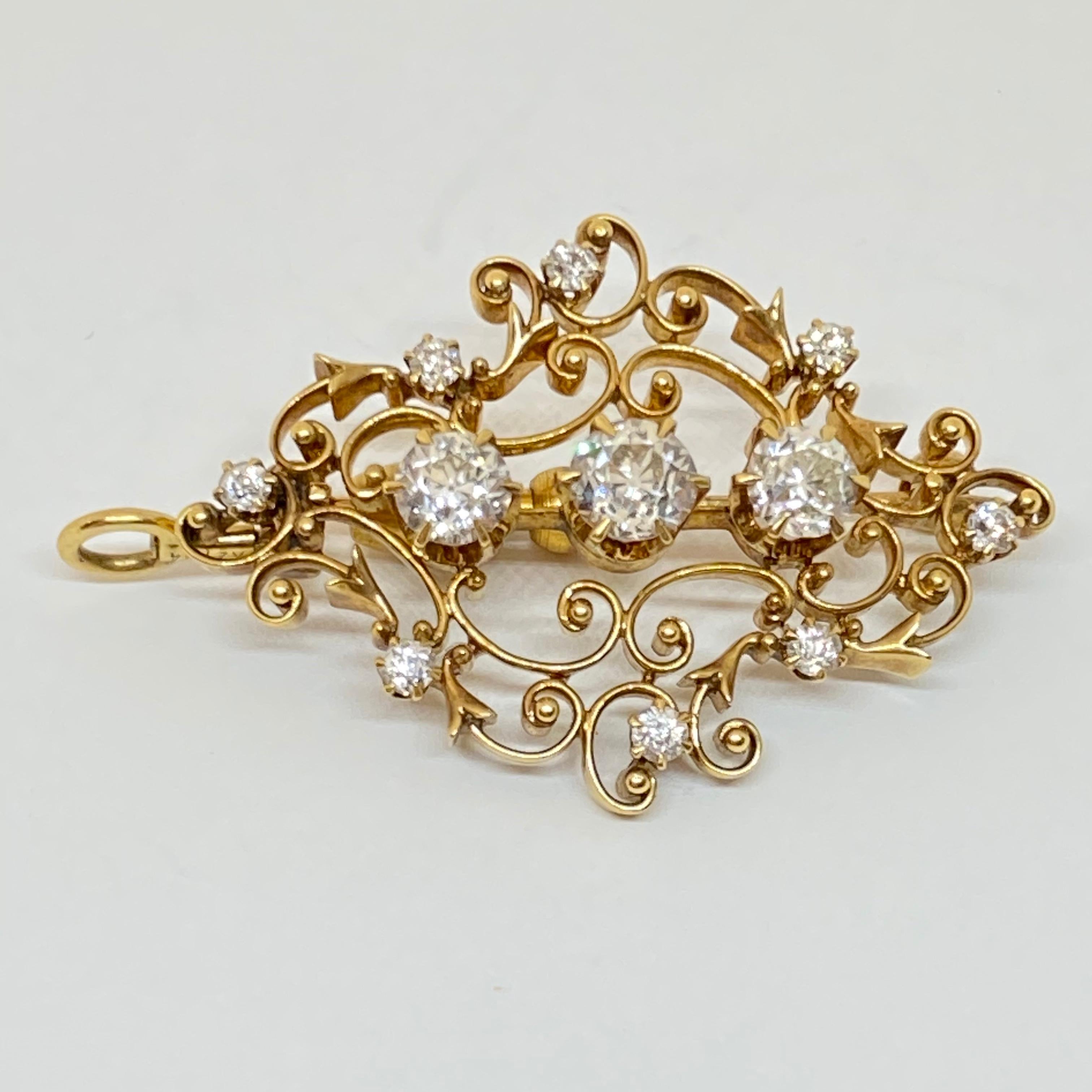 This elegant estate brooch is fashioned from 18K yellow gold. The brooch is a delicate scroll design. There are three old European cut diamonds set in six-prong heads. There are eight additional old European cut diamonds scattered around the brooch