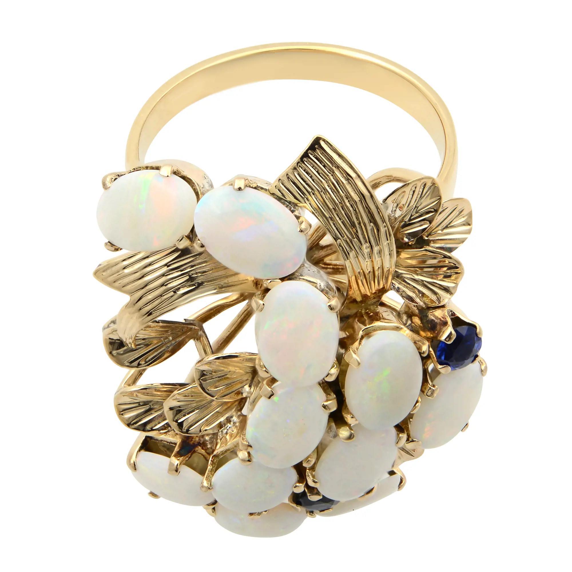 This stunning estate cocktail ring comes with a flashy statement look. A must have in your jewelry collection. The ring is crafted in 14K yellow gold. Features 11 prong set oval shaped white Opal and 2 round cut blue Sapphires. Ring size 7. Total