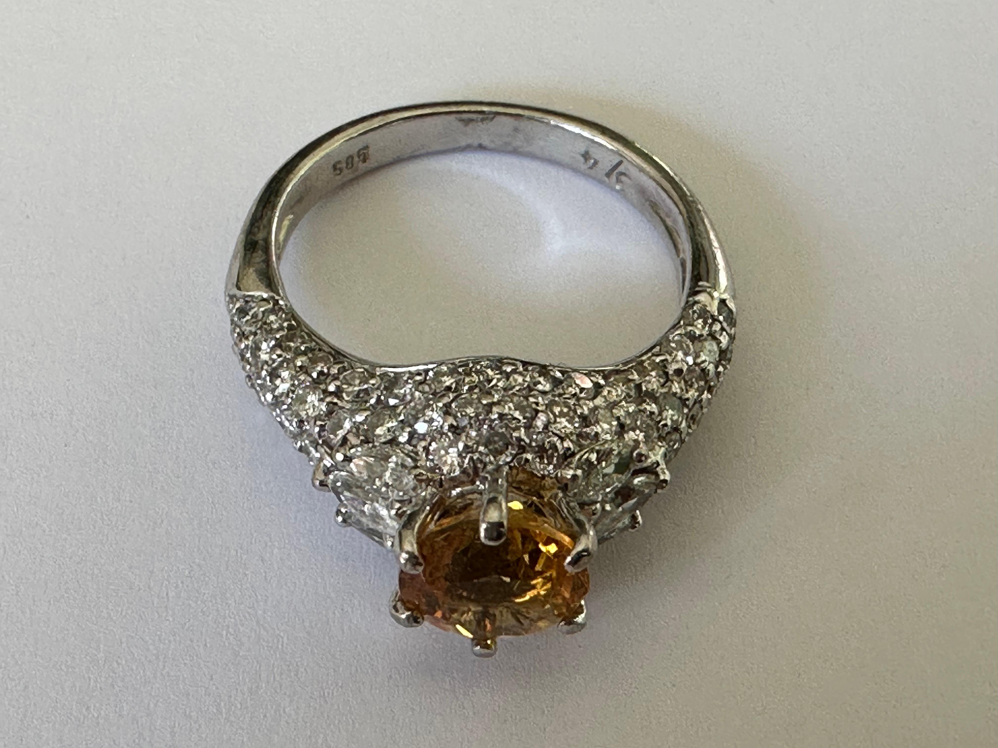 This beautiful round-shaped 6.5mm orange-yellow sapphire center stone is accented by approximately 0.75 carats of pavé set round brilliant-cut and marquise diamonds and set in 14K white gold.

