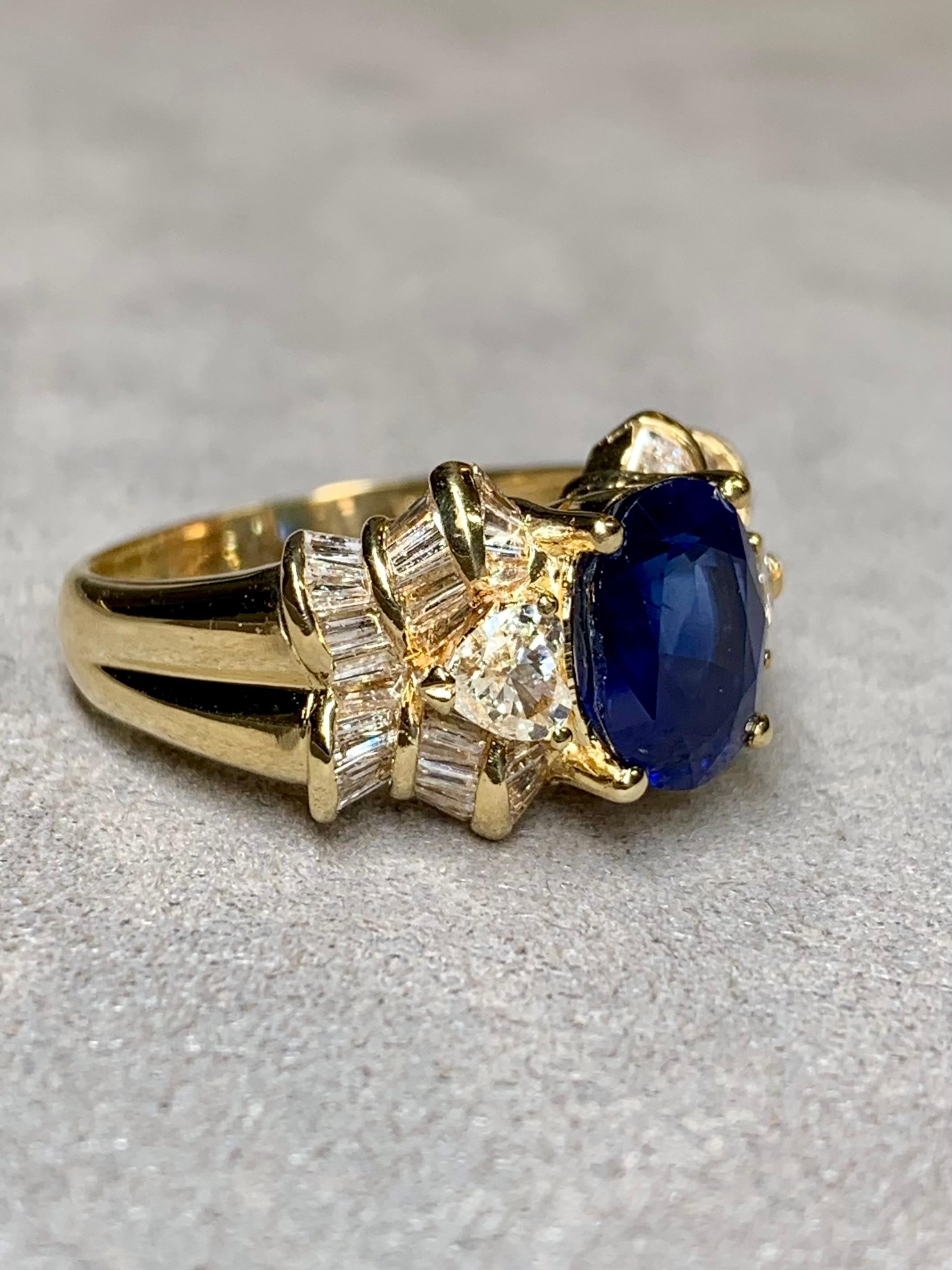An impressive cocktail ring done in 18K yellow gold and centered by a 2.93ct ( known weight) oval cut natural sapphire (heat only). It has gorgeous color when lit correctly but does tend to be a bit on the darker side. Flanking the sapphires is