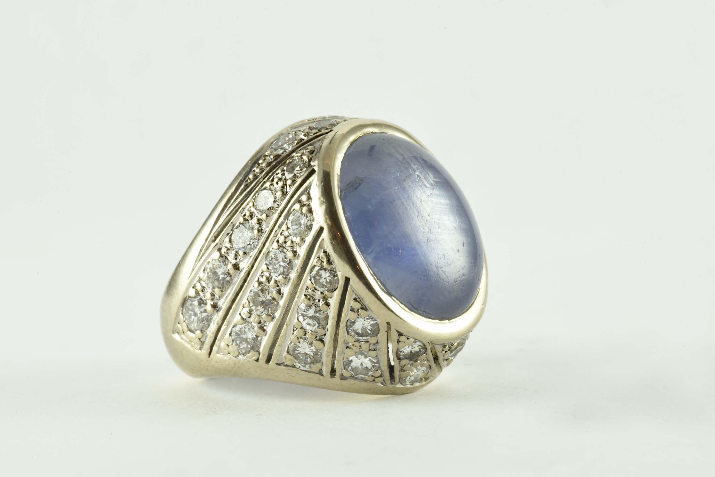 This natural oval-shaped cabochon pale blue star sapphire measuring 14 X 12mm is surrounded on all sides by thirty-six round diamonds in diagonal rows totaling approximately 1.50 carats, G-H color, SI1 clarity and mounted in 18 karat white gold. 
