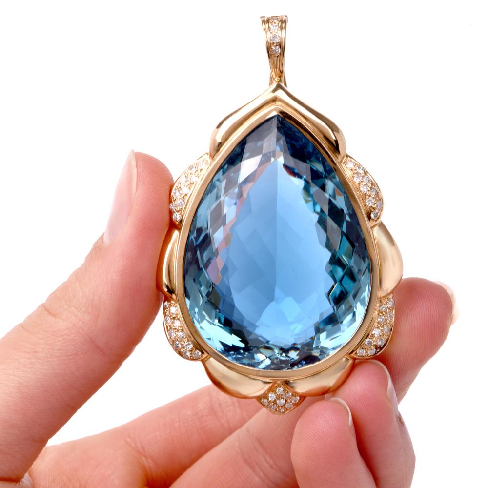 This impressive and opulent estate pendant necklace exposes a sizable 125.34 carat pear-shape blue Topaz with artfully checkerboard-faceted borders, set within a yellow gold bezel and surrounded by a highly ornate, diamond-studded frame with