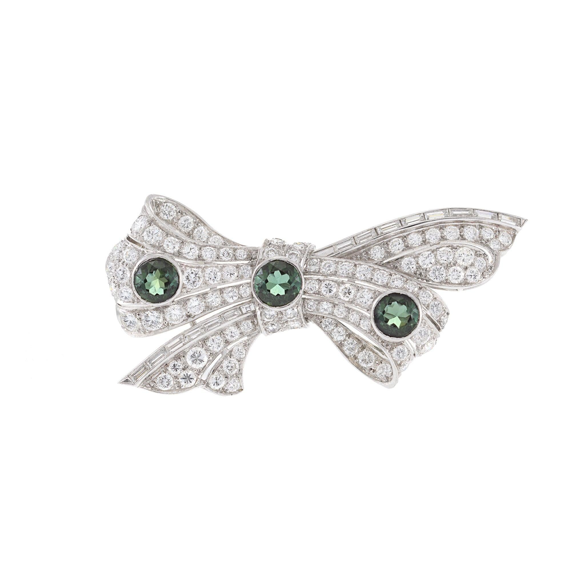 This Estate Platinum Art Deco Period Diamond and Garnet Bow Pin is a stunning example of Art Deco design. The pin features 4.00 carats total weight of F-G VVS/VS round and baguette cut diamonds and 1.60 carats total weight of round cut green