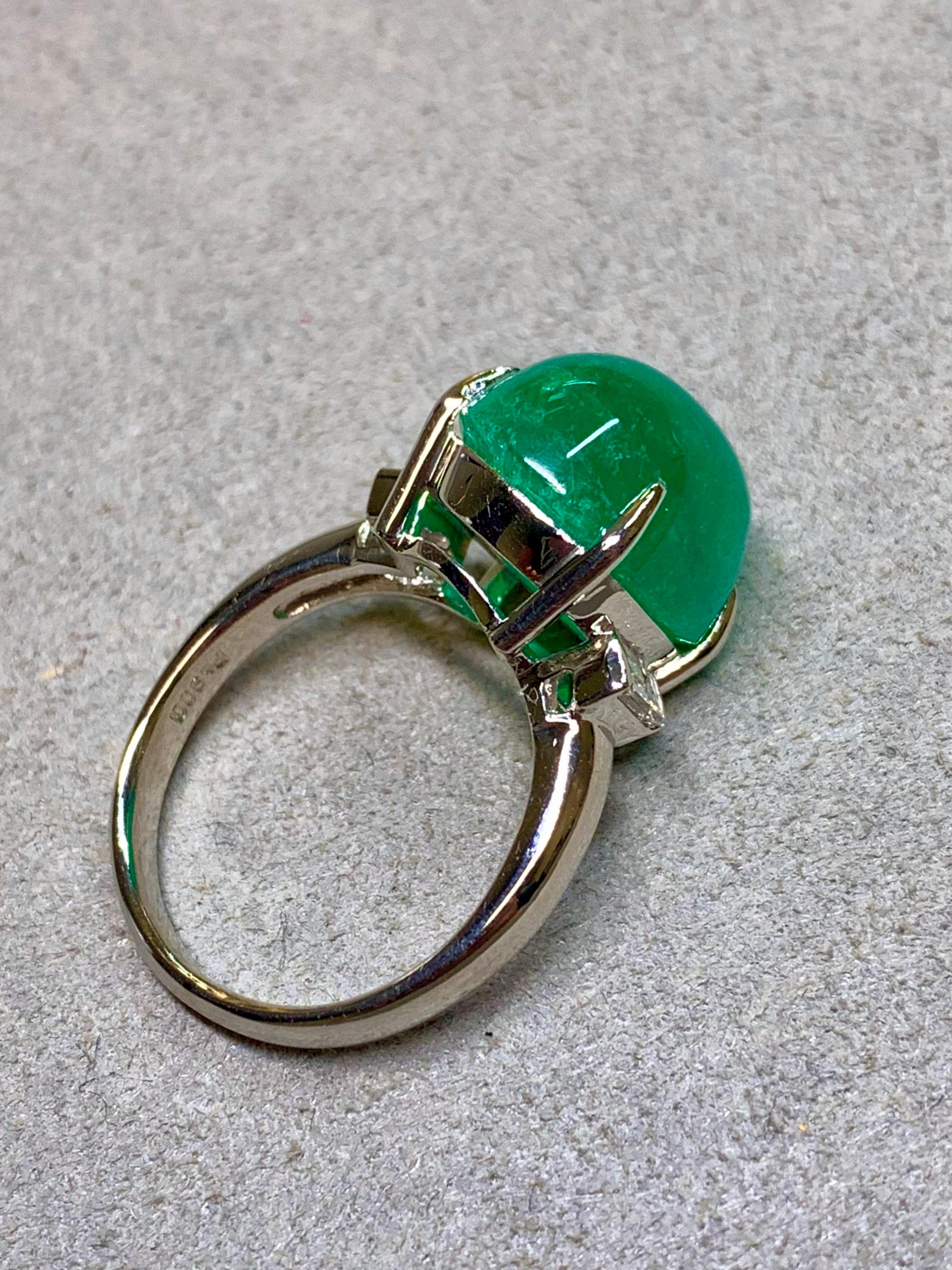 
An impressive vintage platinum three-stone ring, centered by a glowing cabochon emerald weighing 11.53 carats. The emerald shows a vivid, saturated green color and is flanked on each side by matched baguette-cut diamonds. The diamonds total