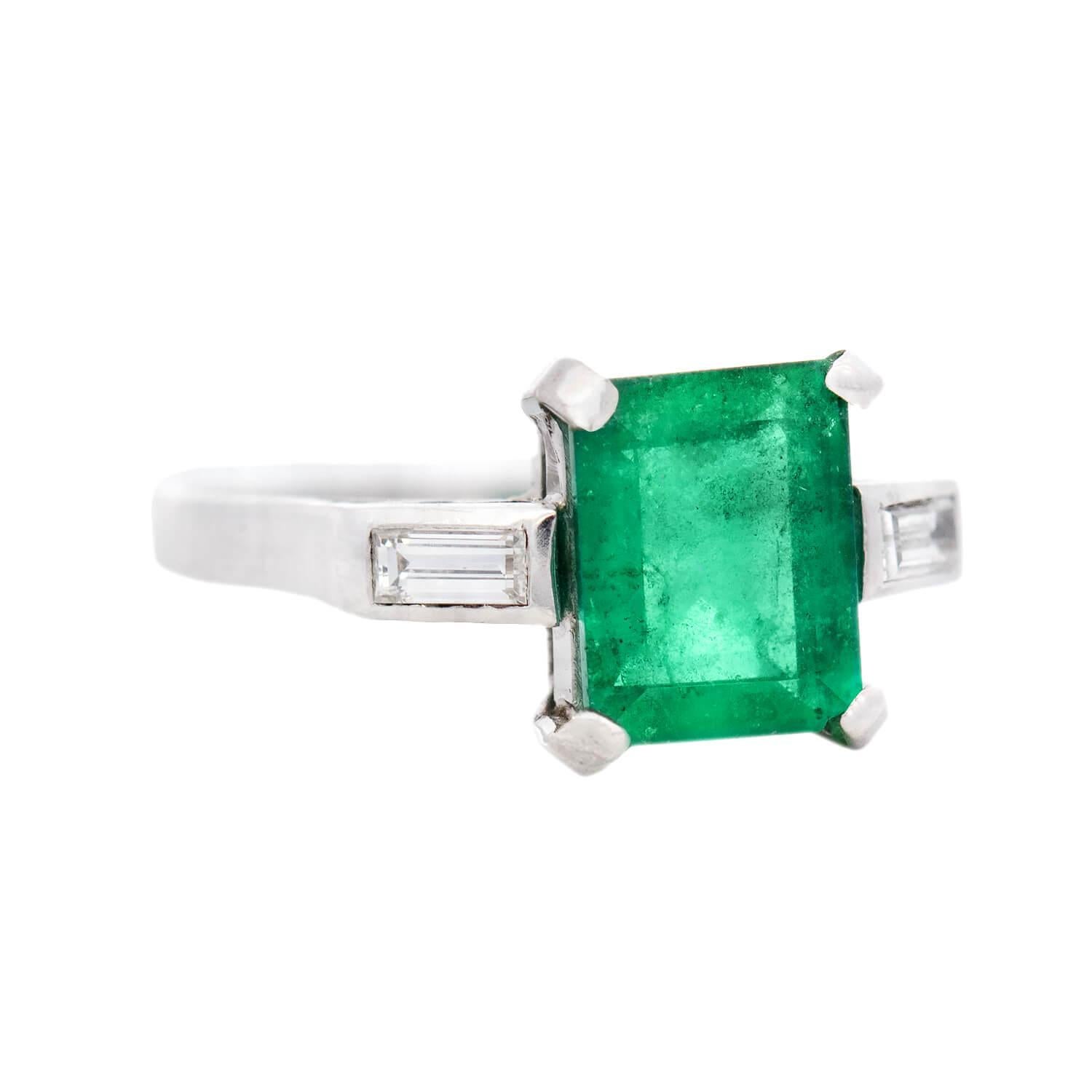 Uno splendido anello con smeraldo e diamante! Realizzato in platino, questo anello presenta tre pietre che attraversano orizzontalmente la parte anteriore dell'anello. La pietra centrale è uno smeraldo di taglio rettangolare da 1,50 carati, che