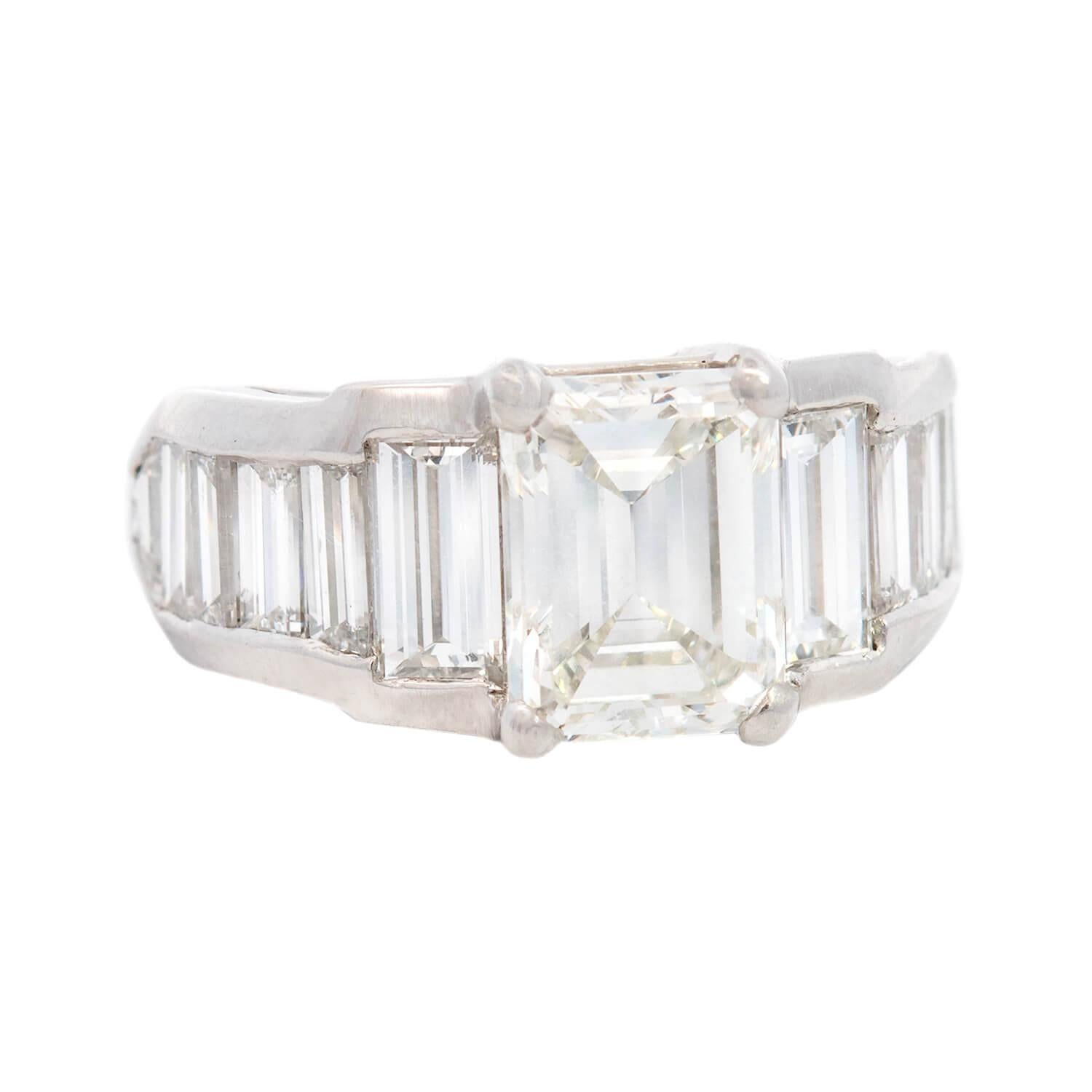 ¡Un precioso anillo de compromiso de diamantes! Elaborado en platino, este sustancioso anillo presenta un diamante central talla esmeralda, con un peso en quilates de 3 ct. La piedra presenta color I y claridad VS1. Los hombros del anillo presentan