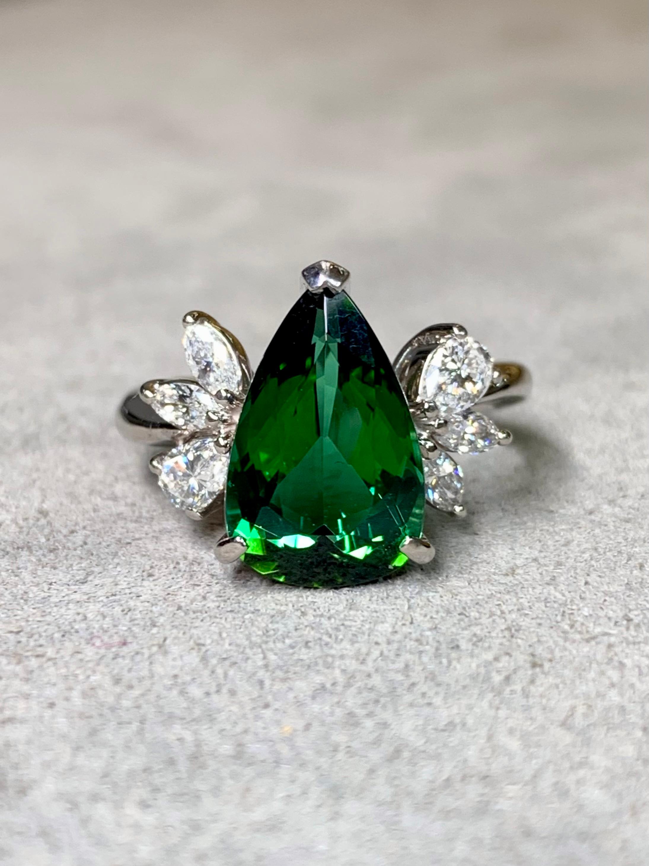 An exceptional estate ring crafted in platinum, centered by a vivid 3.97-carat natural green pear-shaped tourmaline. The center stone is flanked by a total of 0.61 carats of fine F–G color, VS1 clarity marquise and pear-shaped diamonds, all expertly