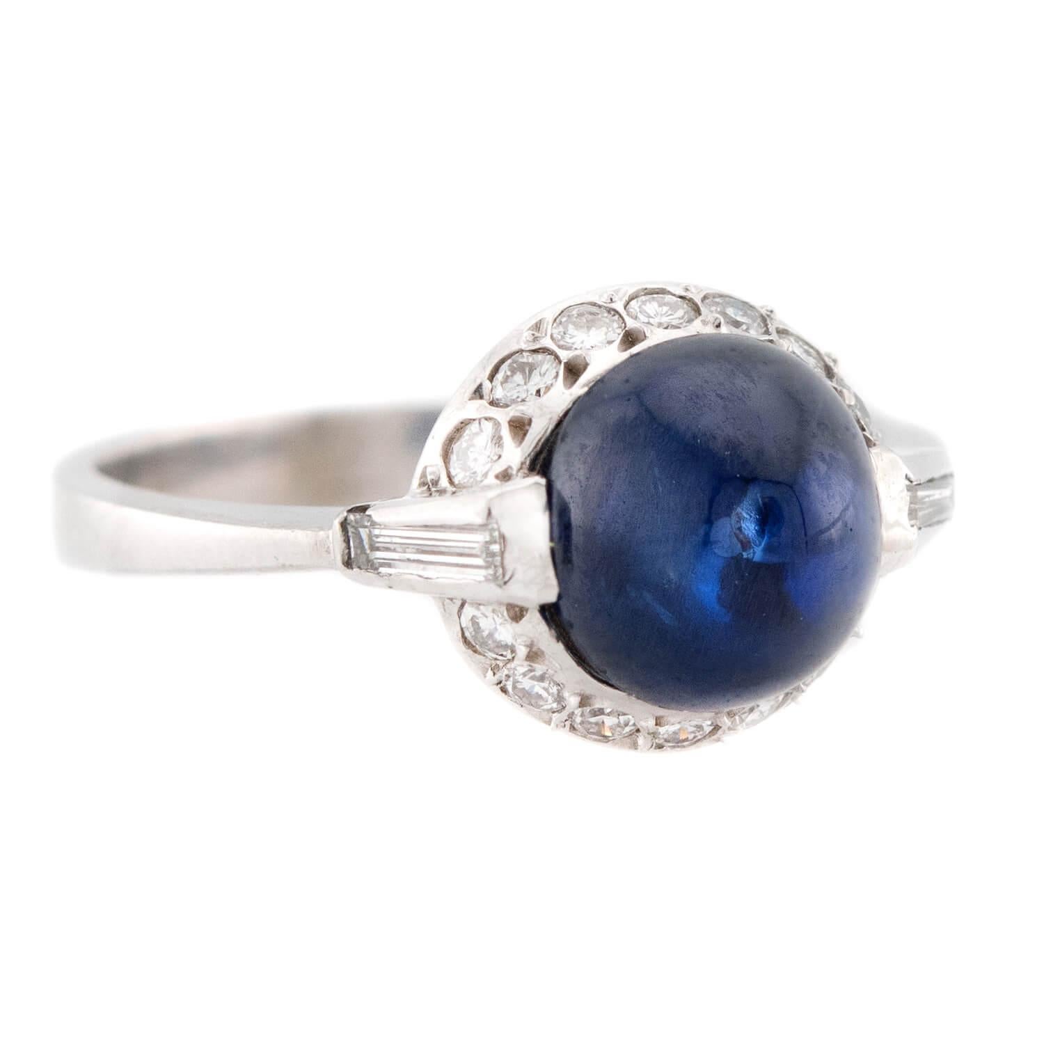A beautiful sapphire and diamond halo ring! Crafted in platinum, this ring features a central sapphire bullet cabochon, which has a carat weight of 1.35ct. The cabochon is held within a bezel-setting and displays a deep blue hue. The sapphire is