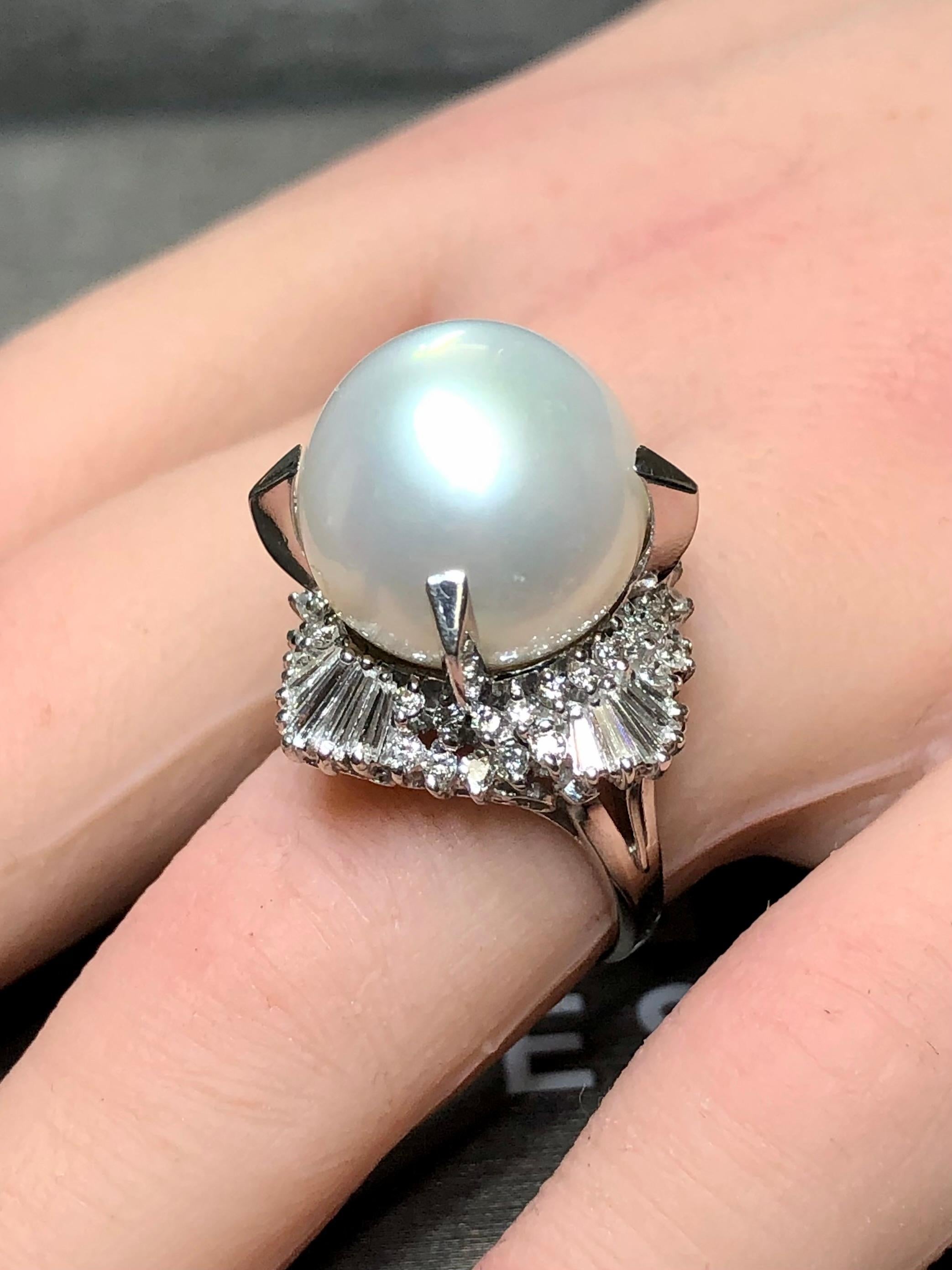 Un anello da cocktail grande e imponente, centrato da una perla bianca dei Mari del Sud incastonata con 14,75 mm, con un leggerissimo sottotono argentato, che mostra una lucentezza uniforme e una minima corrosione superficiale. La perla è circondata