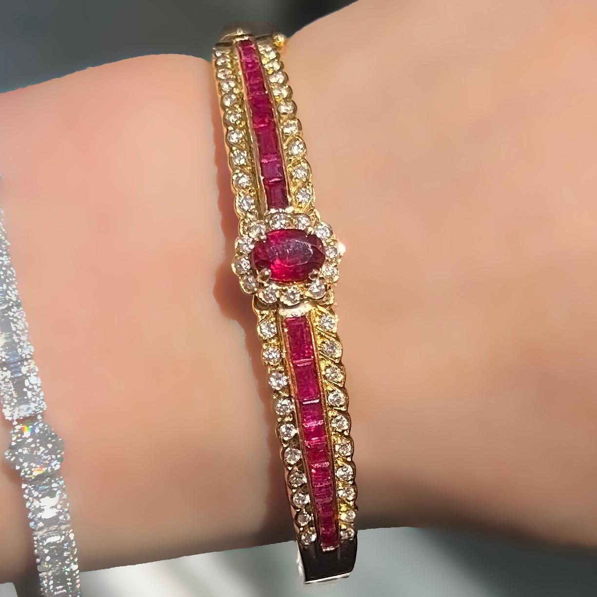 18-karat yellow gold vintage estate ruby and diamond retro-hinged bangle bracelet.
The center stone is an oval-shaped red ruby. Delicately handset and cut are invisibly set baguette-shaped ruby gemstones. The beauty of these rubies is the slight