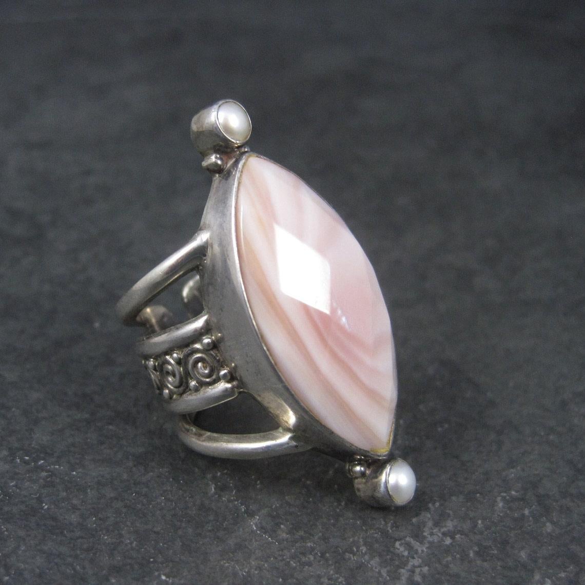 This gorgeous ring is a product of Sajen.
It is sterling silver and features a huge 16x31mm faceted pink mother of pearl accented by 4mm pearls.

The face of this ring measures 1 11/16 inches north to south.
The band tapers from 7/8 to 1/2 of an