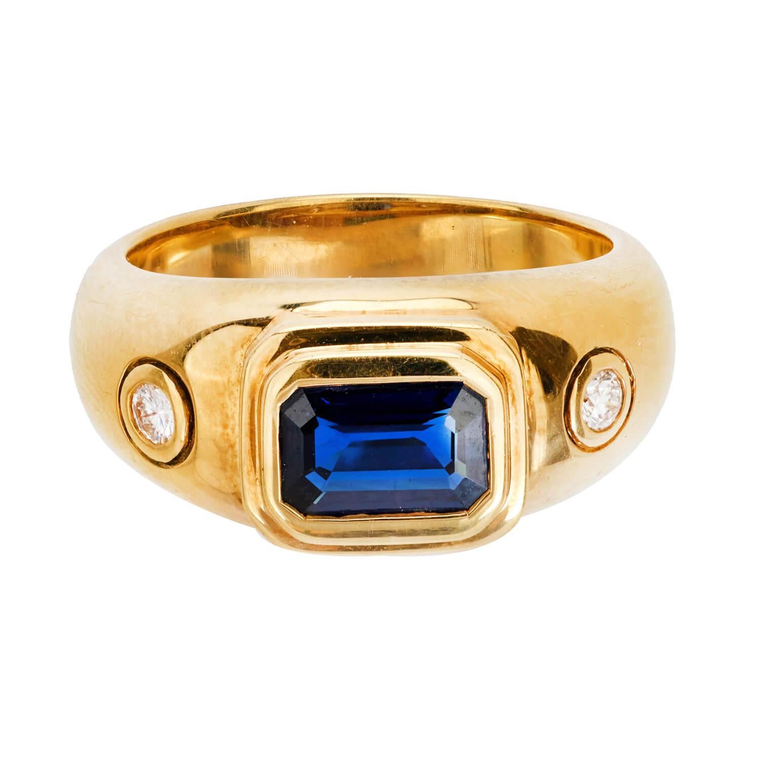 A beautiful sapphire and diamond ring! Crafted in 18k yellow gold, this ring features a central 1.5ct emerald cut sapphire. The stone is held within a smooth and simple bezel setting, and displays a lovely deep, rich blue hue. The sapphire is