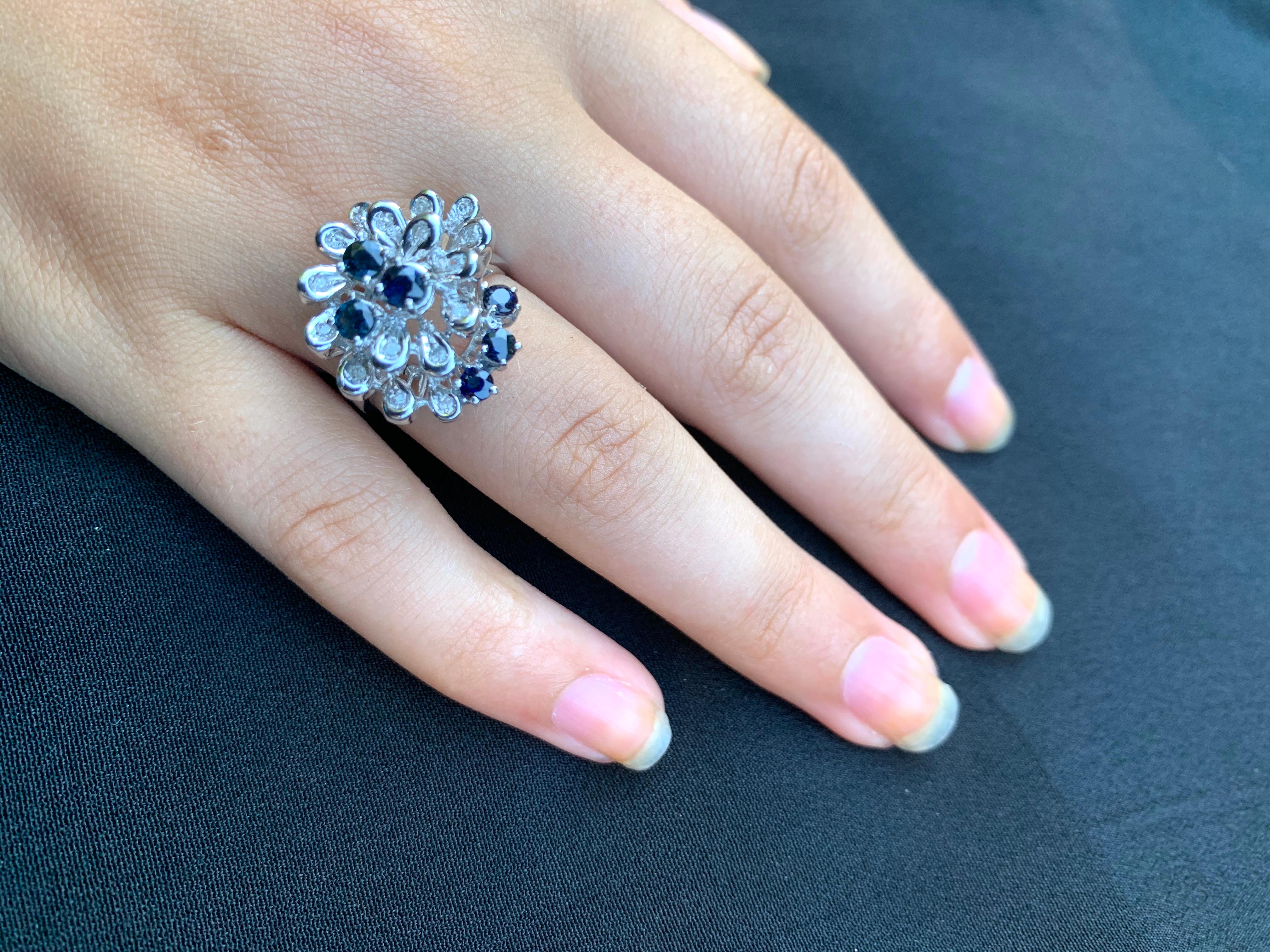 Anillo de cóctel en oro blanco de 18 quilates con forma de flor grande y preciosa de diamante y zafiro 
Segunda mitad del siglo XX.
Este hermoso anillo presenta finos zafiros azul oscuro y diamantes blancos compuestos en forma de una gran flor poco