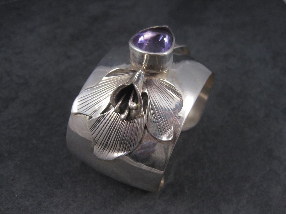 Dieses wunderschöne Manschettenarmband im Vintage-Stil besteht aus Sterlingsilber.
Der 15x20 mm große Amethyst im Birnenschliff ist eine Kreation der berühmten Carol Felley.

Dieses Armband ist 1 1/2 Zoll breit.
Er hat einen Innenumfang von 6 1/4