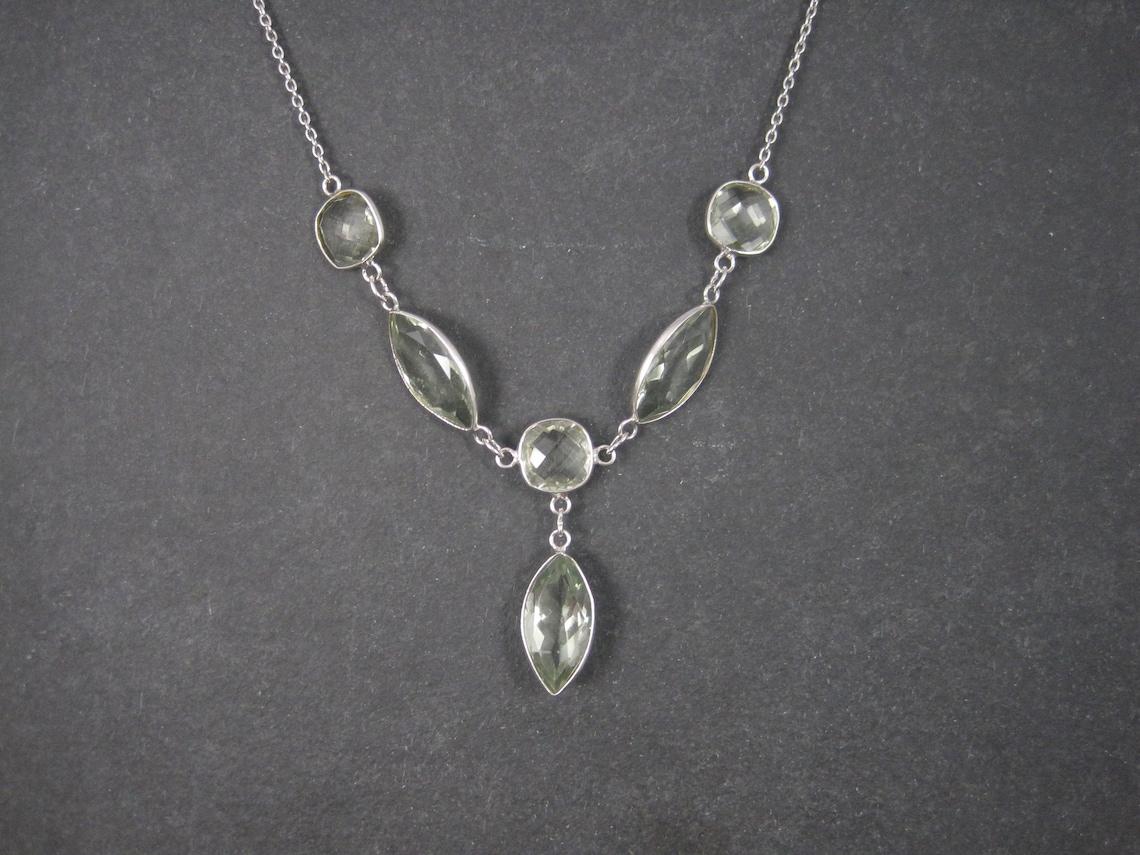 This beautiful estate necklace is sterling silver.
It features an estimated 24 carats in stunning, light green amethyst gemstones.

It is adjustable from 18 and 19 inches.

Marks: 925

Excellent condition