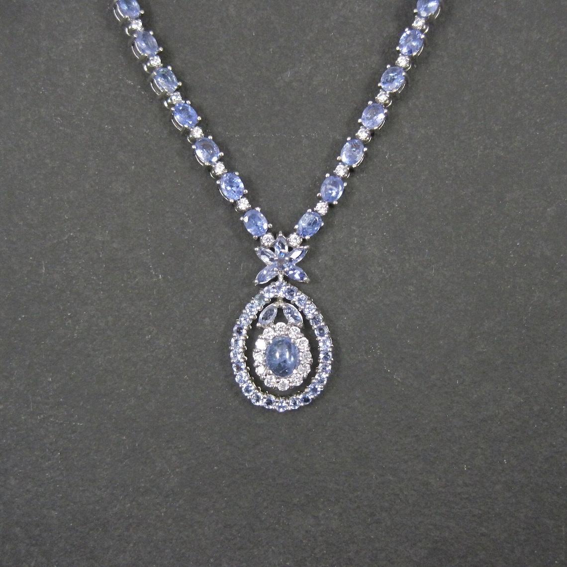 This stunning estate necklace is sterling silver.
It features tanzanites in a combination of 54 oval cut 4x6mm, 7 marquise cut 3x5mm, 29 round cut 2.5mm, and a single oval cabochon cut measuring 6x8mm.
The accent stones are cubic zirconia.

Note