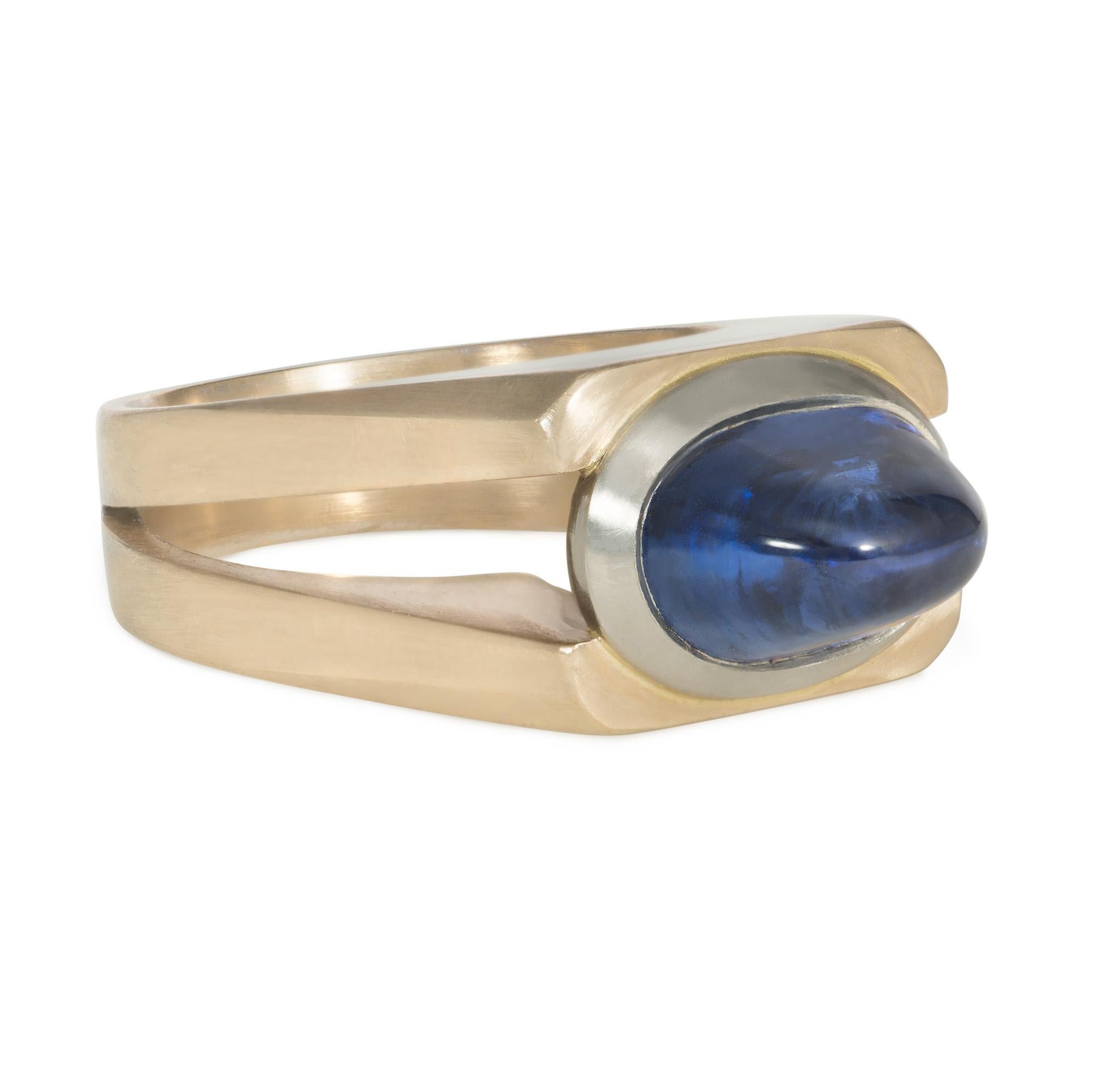 An estate sapphire and two-color gold ring of streamlined industrial design, centered by a sugarloaf cabochon sapphire in a white-gold bezel, and set in a brushed yellow-gold mount with tapering open shoulders, in 18k.  Atw sapphire 5.57 cts. 