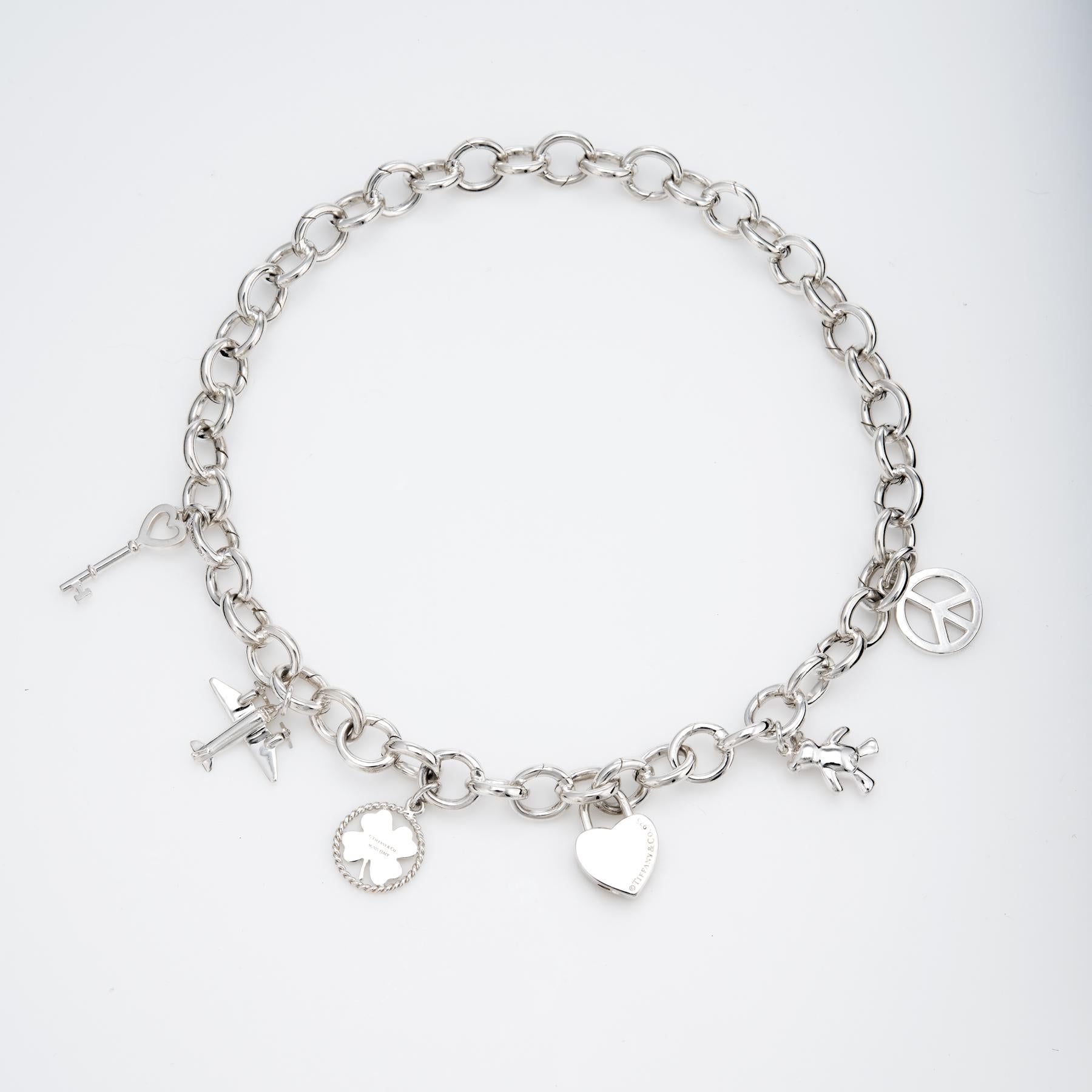 Elegant and finely detailed pre owned Tiffany & Co multi charm necklace, crafted in 925 sterling silver.  

The necklace features 6 charms: heart key, airplane, clover, heart lock, teddy bear and peace sign. Each link on the necklace features an