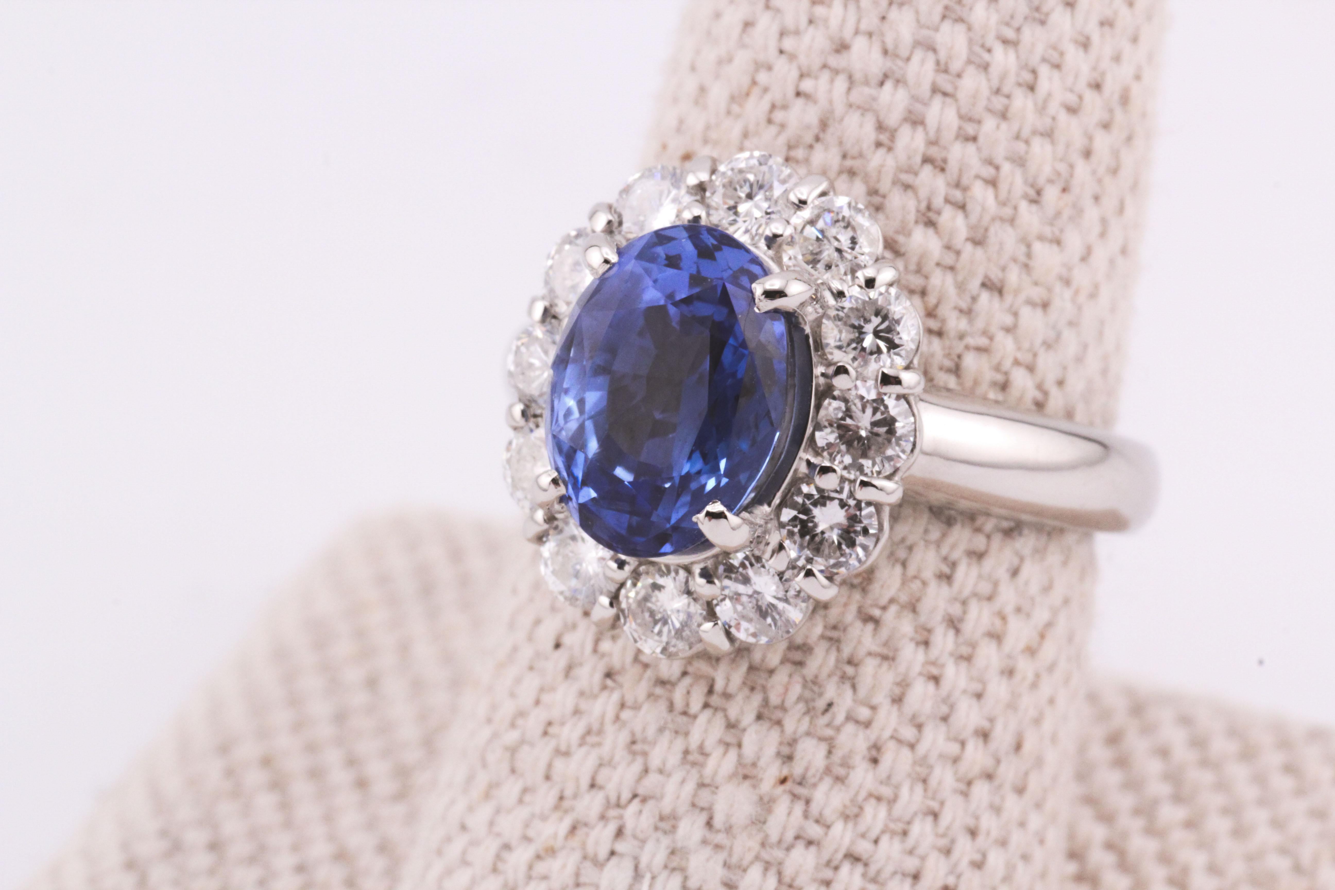 This Estate Unheated Sapphire and Diamond Halo Ring is a masterpiece of timeless elegance and rare beauty. At its heart lies a stunning 3.83-carat oval-cut sapphire, boasting a vibrant cornflower blue hue that captivates with its natural, unheated