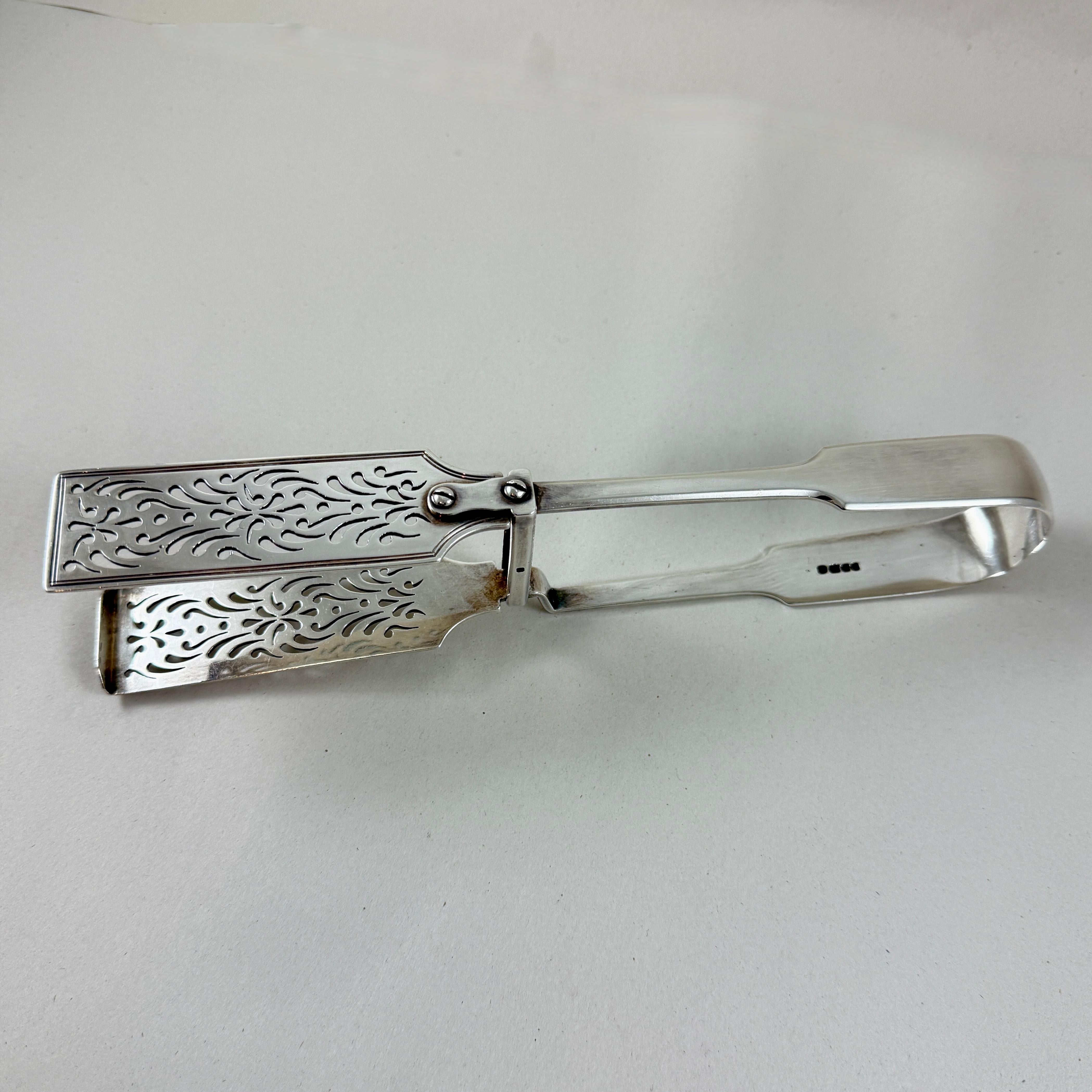 De la época victoriana, una pinza maestra inglesa de plata de ley para servir espárragos. Londres, hacia 1838,

En patrón de violín, con hojas bellamente ornamentadas y perforadas a mano, una de ellas con un labio elevado para agarrar fácilmente los
