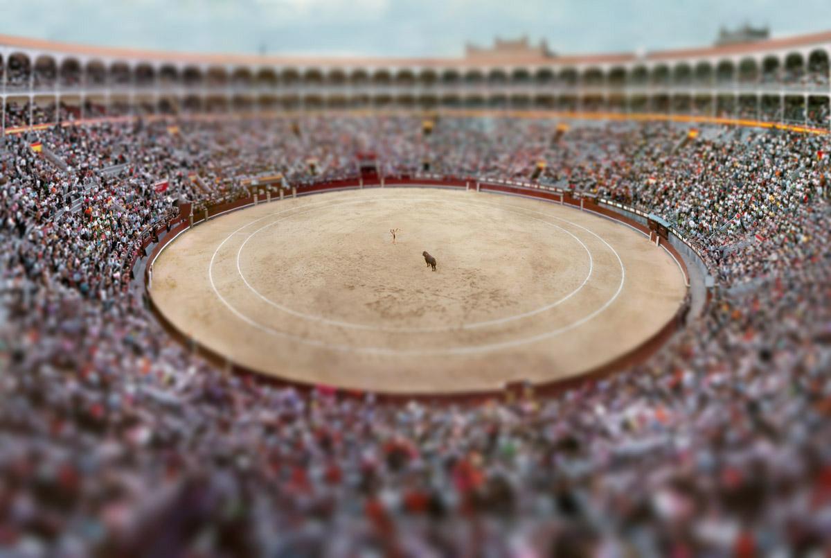 Las Ventas #2 by Esteban Pastorino Diaz depicts a bull fighting ring in Madrid, Spain. The matador and bull stand in the center of the ring, waiting in anticipation for the other to make a move.  People fill the seats of the arena, crowding the