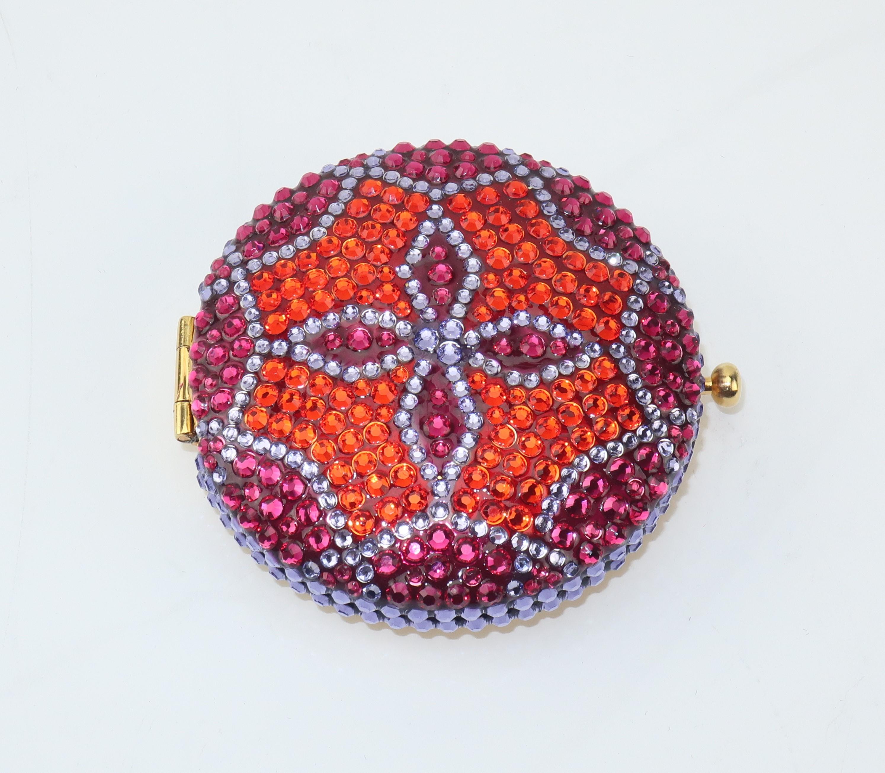 A collectible powder compact by handbag designer Kathrine Baumann for Estee Lauder with a pave crystal snowflake design in shades of red, magenta and lilac all set in a jewelry quality gold tone metal.  The push button closure opens to reveal a