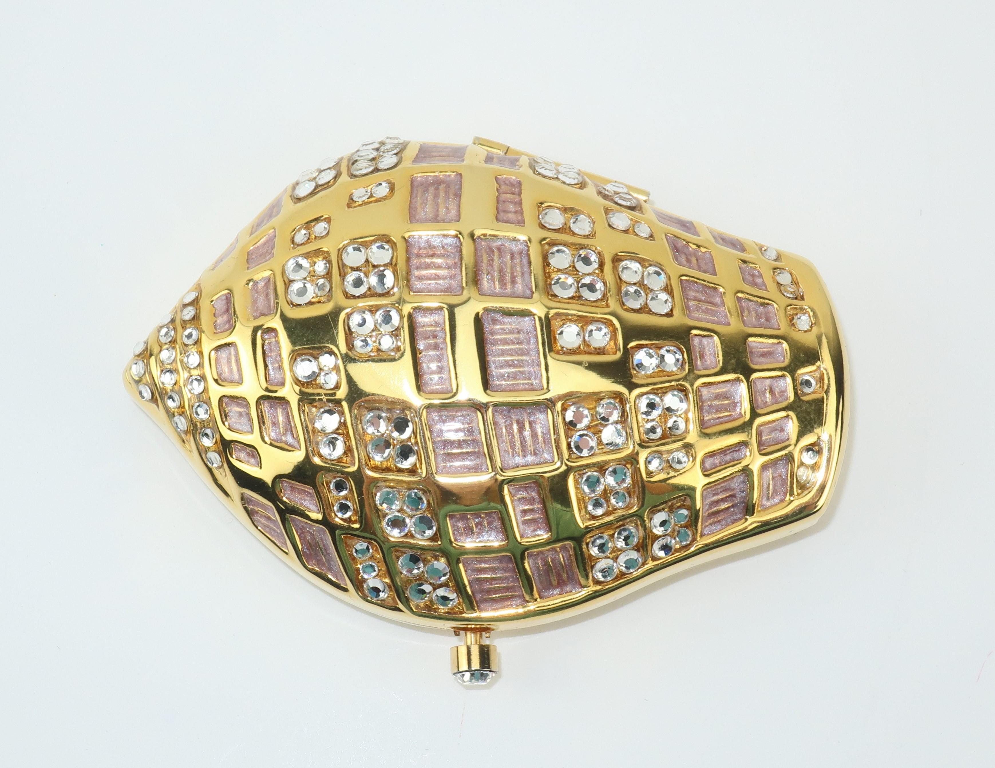 A collectible powder compact from Estee Lauder in the form of a shell with crystal rhinestone embellishments and sparkling pink enamel decoration.  The crystal rhinestone push button closure opens to reveal a mirror and a refillable pressed powder