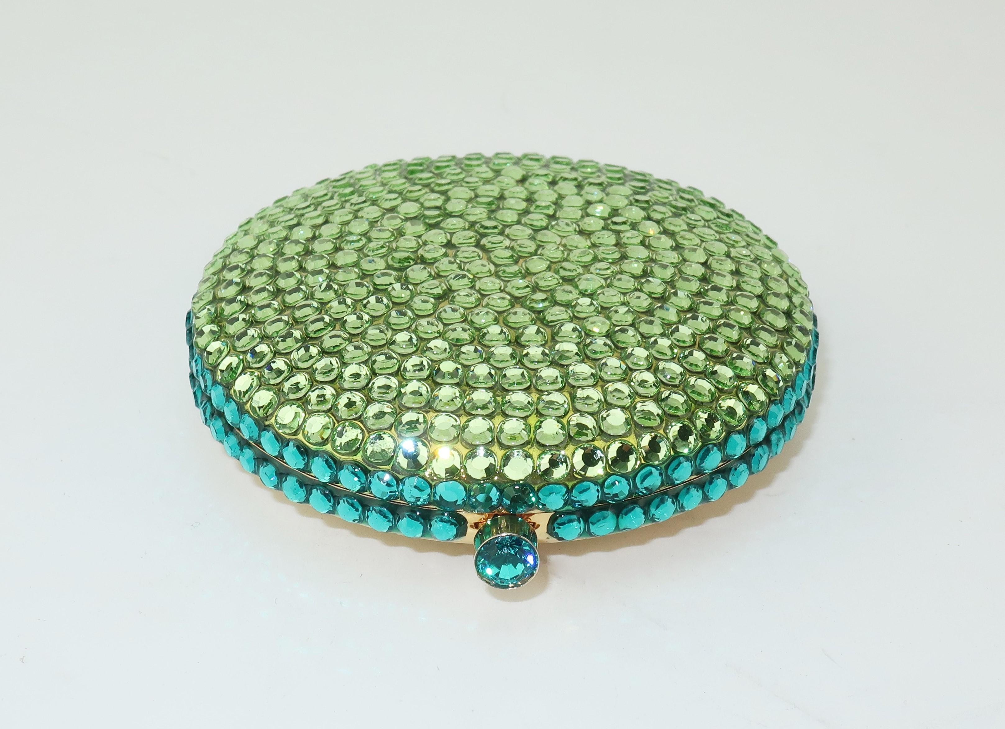 A collectible powder compact by Estee Lauder resembling a yummy macaroon in a vibrant spring green and aqua blue combination all set in a jewelry quality gold tone metal.  The jeweled push button closure opens to reveal a mirror and a refillable