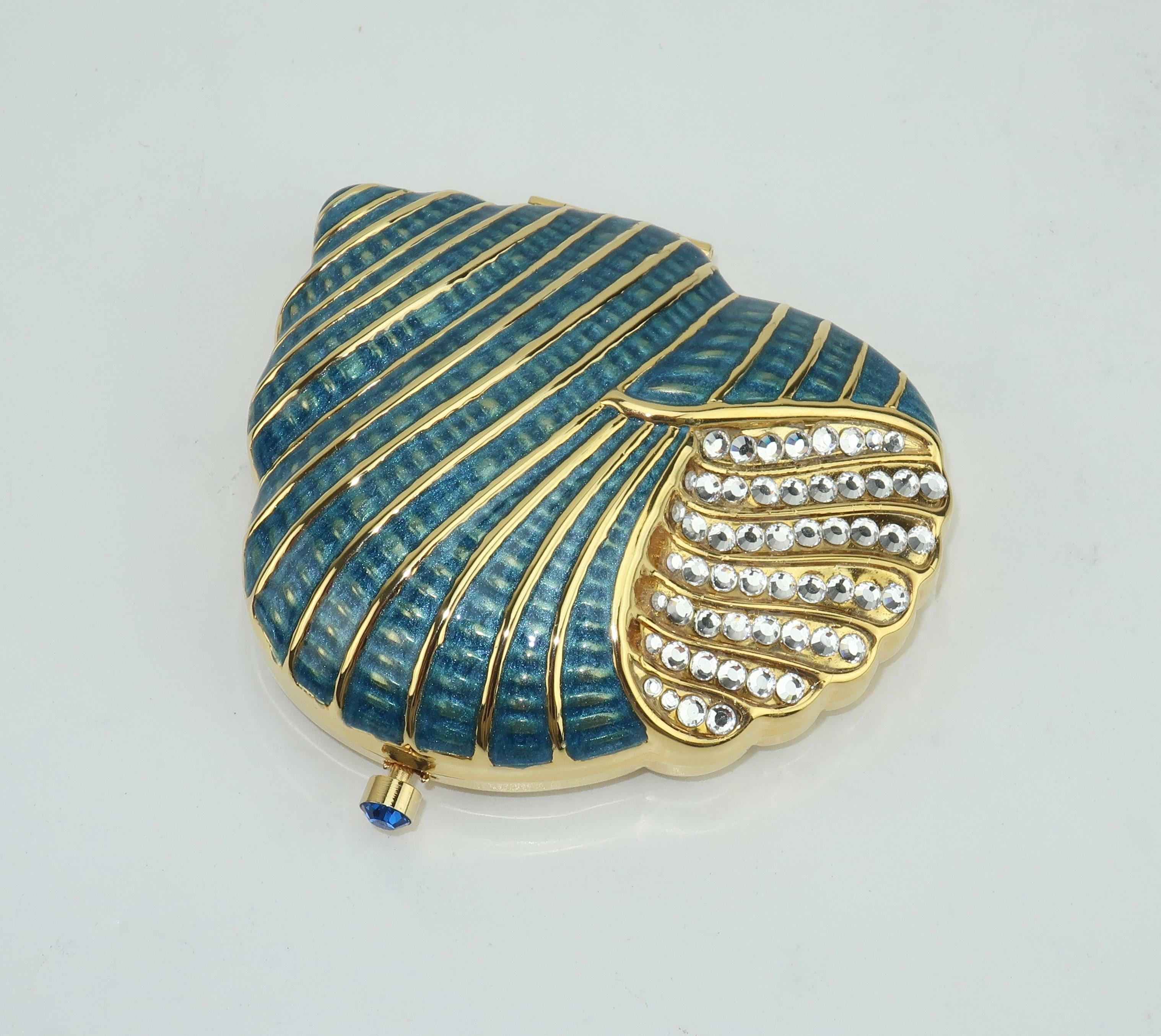 Estee Lauder has been producing limited edition compacts since the 1950's.  This beautiful shell shaped gold tone compact is bedazzled with pave crystals and sea blue enameling.  The rhinestone push button closure opens to reveal a mirror and powder