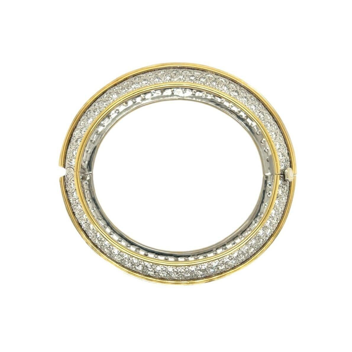An 18 karat yellow and white gold and diamond bracelet, Esther Gallant.  Designed as a hinged bombe bangle decorated around the center with approximately fifty eight  channel set baguette cut diamonds within a yellow gold molding, the outer sides