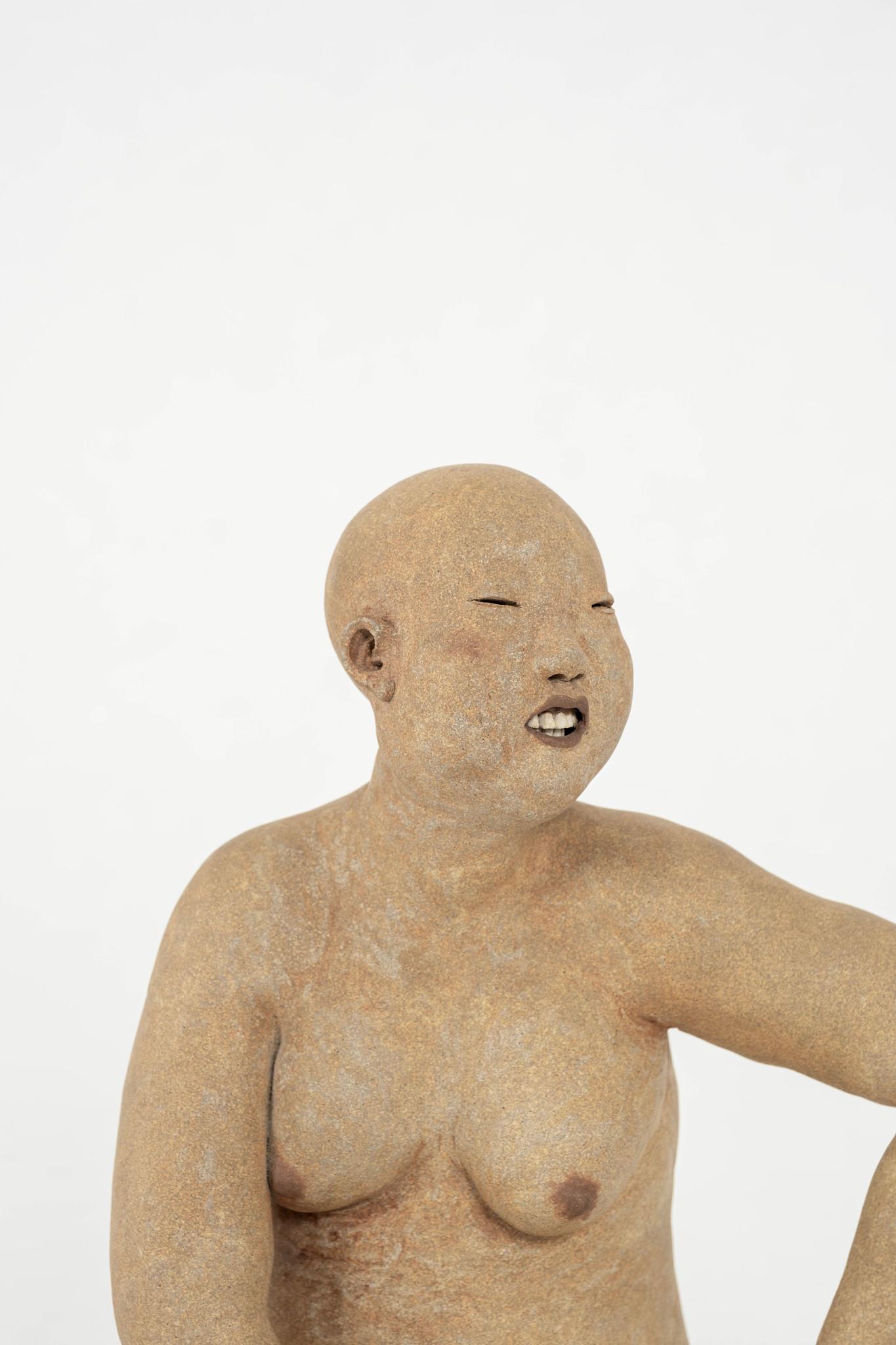 Escultura femenina calva de Esther Shimazu. Utiliza técnicas artesanales para construir figuras de arcilla utilizando engobes coloreados, óxidos al cocerlos, luego los lija a mano y frota con pigmentos para crear una sensación de volumen y color