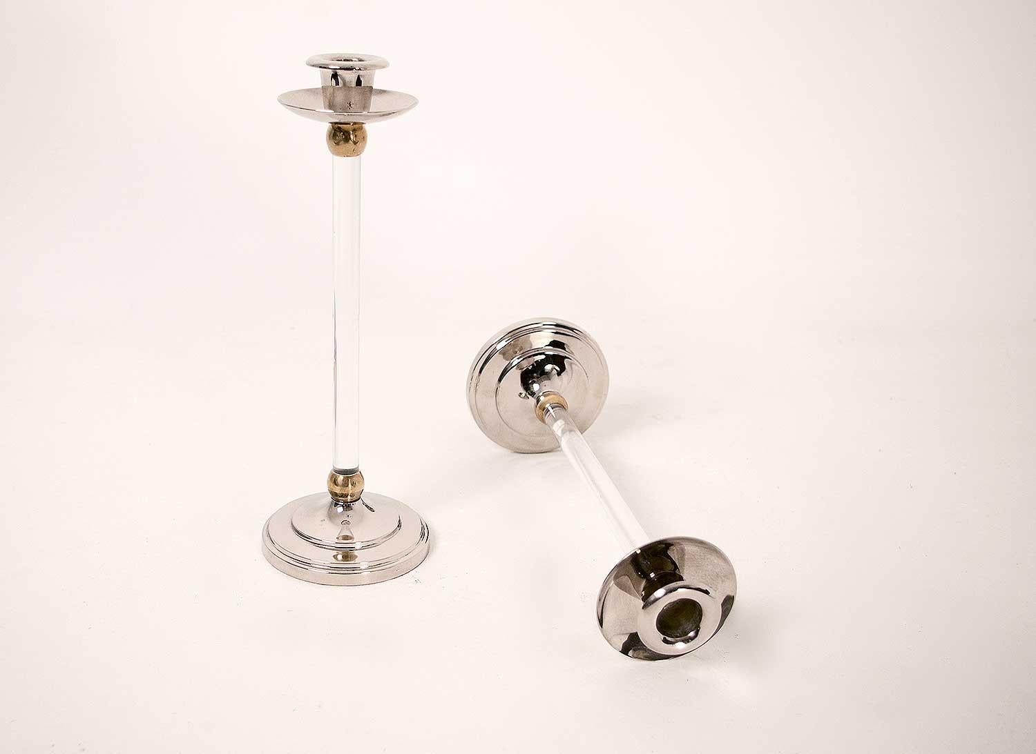 Coppia di candelieri in ottone dorato e argento. Base rotonda modellata con vernice argentata sormontata da un'asta cilindrica in plexiglass con due anelli in ottone dorato a ciascuna estremità. Candelieri rifiniti con coppa e binet in vernice