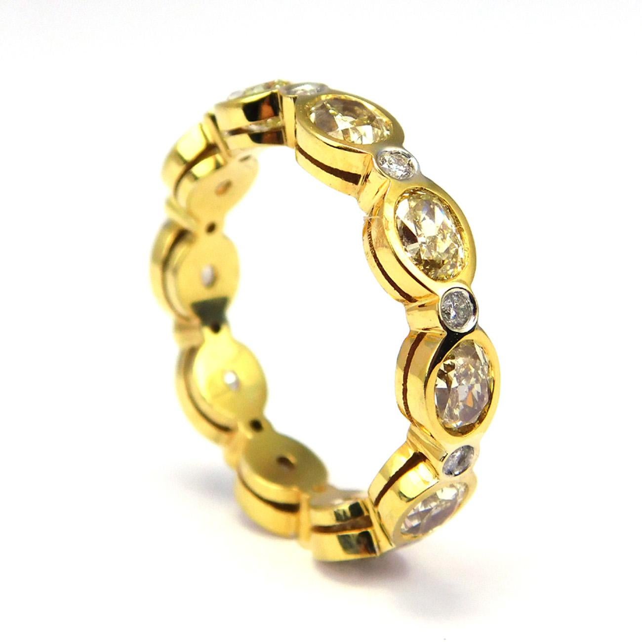 Eternity band in 18K yellow gold with bezel set alternating round and fancy yellow oval cut diamonds. D3.29ct.t.w.